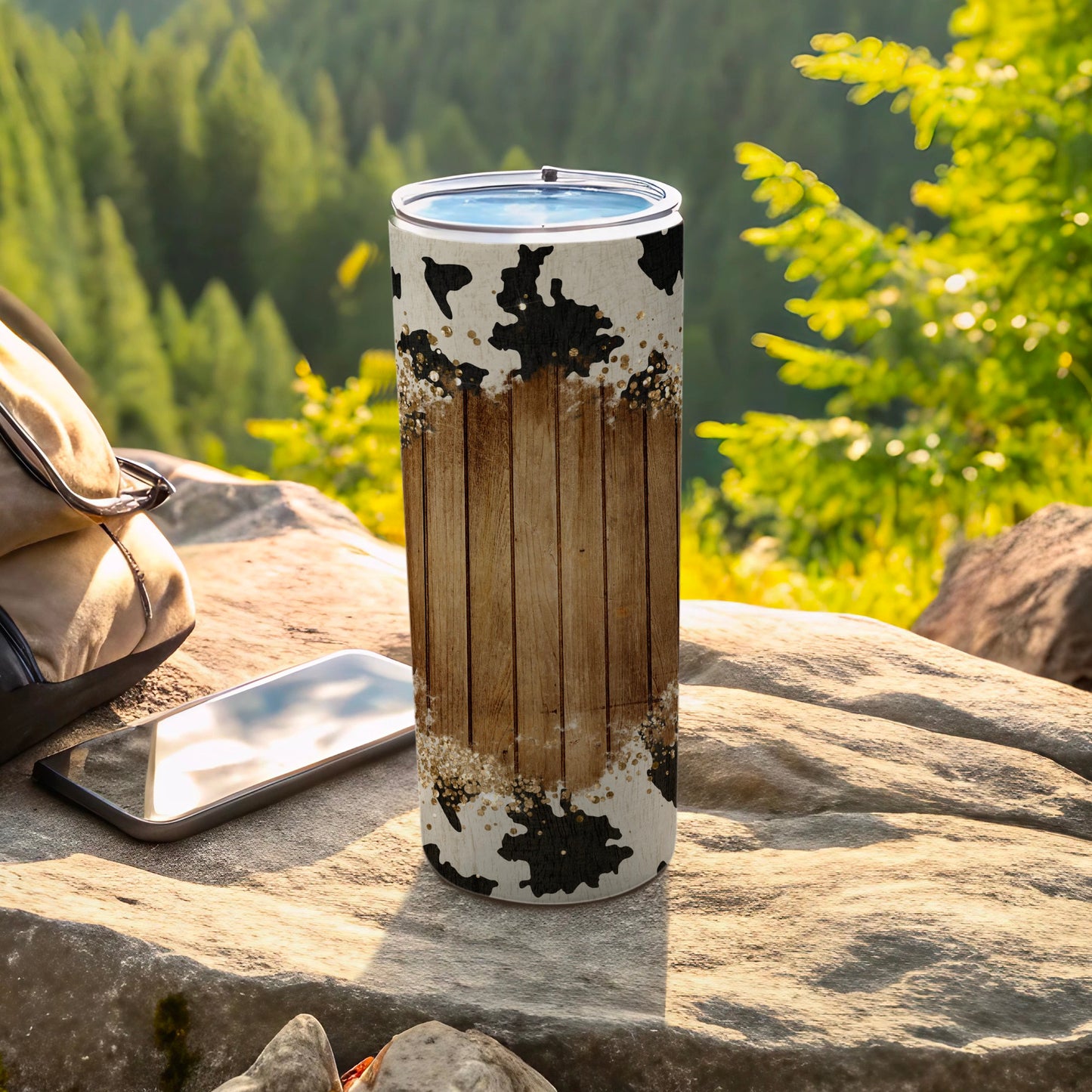 Tall tumbler with cow print and wood grain design on a rock.