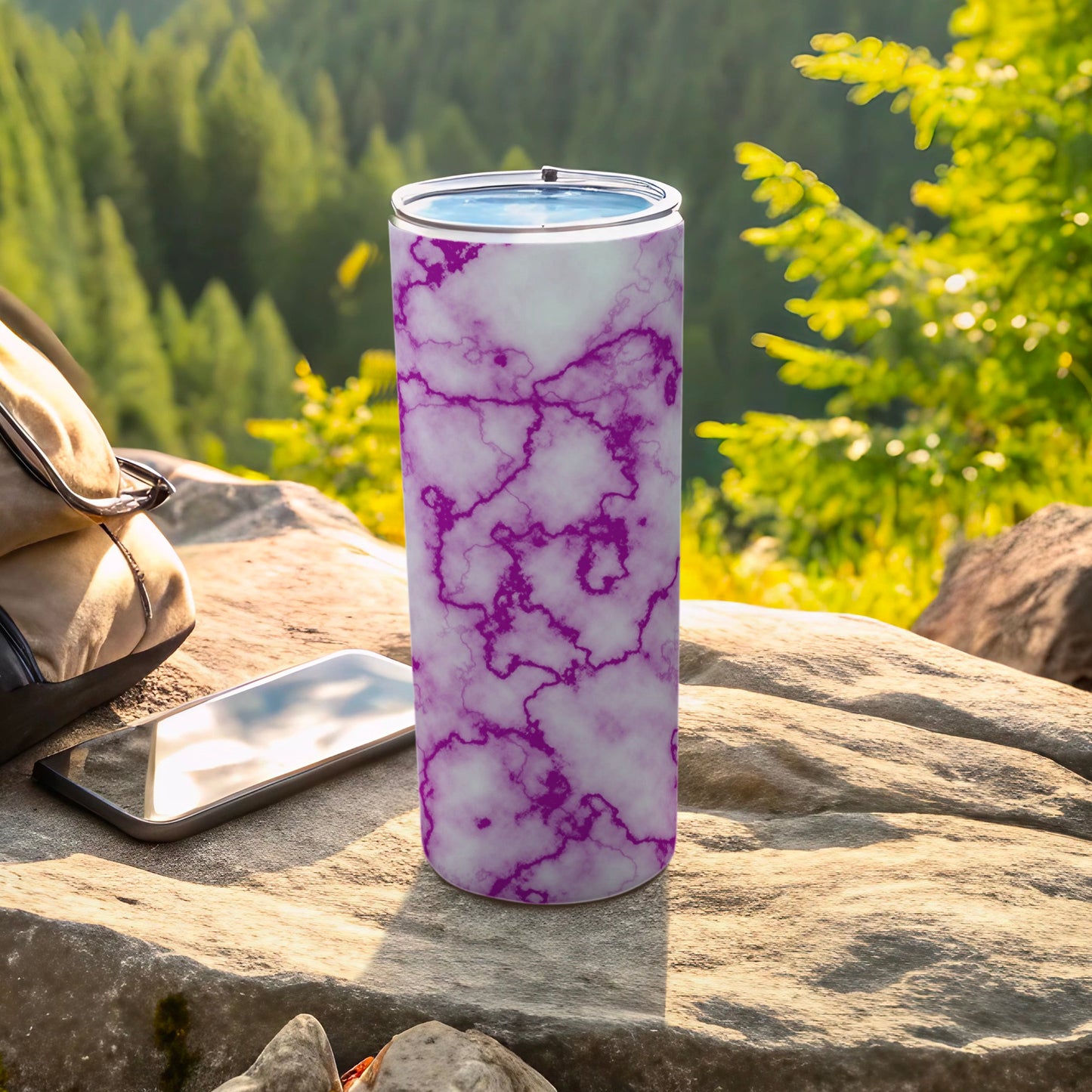 Purple marble patterned tumbler on rock with phone and backpack.
