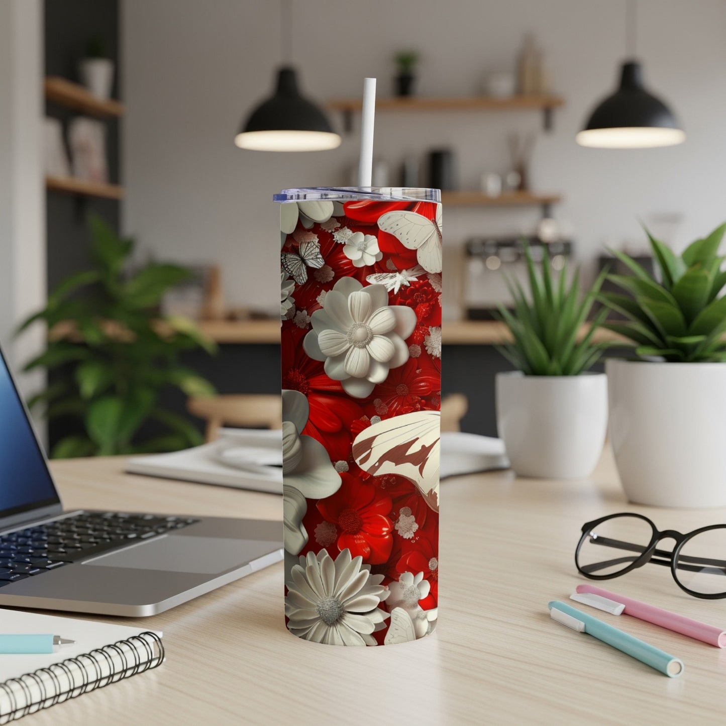 Red tumbler with white floral and butterfly pattern, on a desk.
