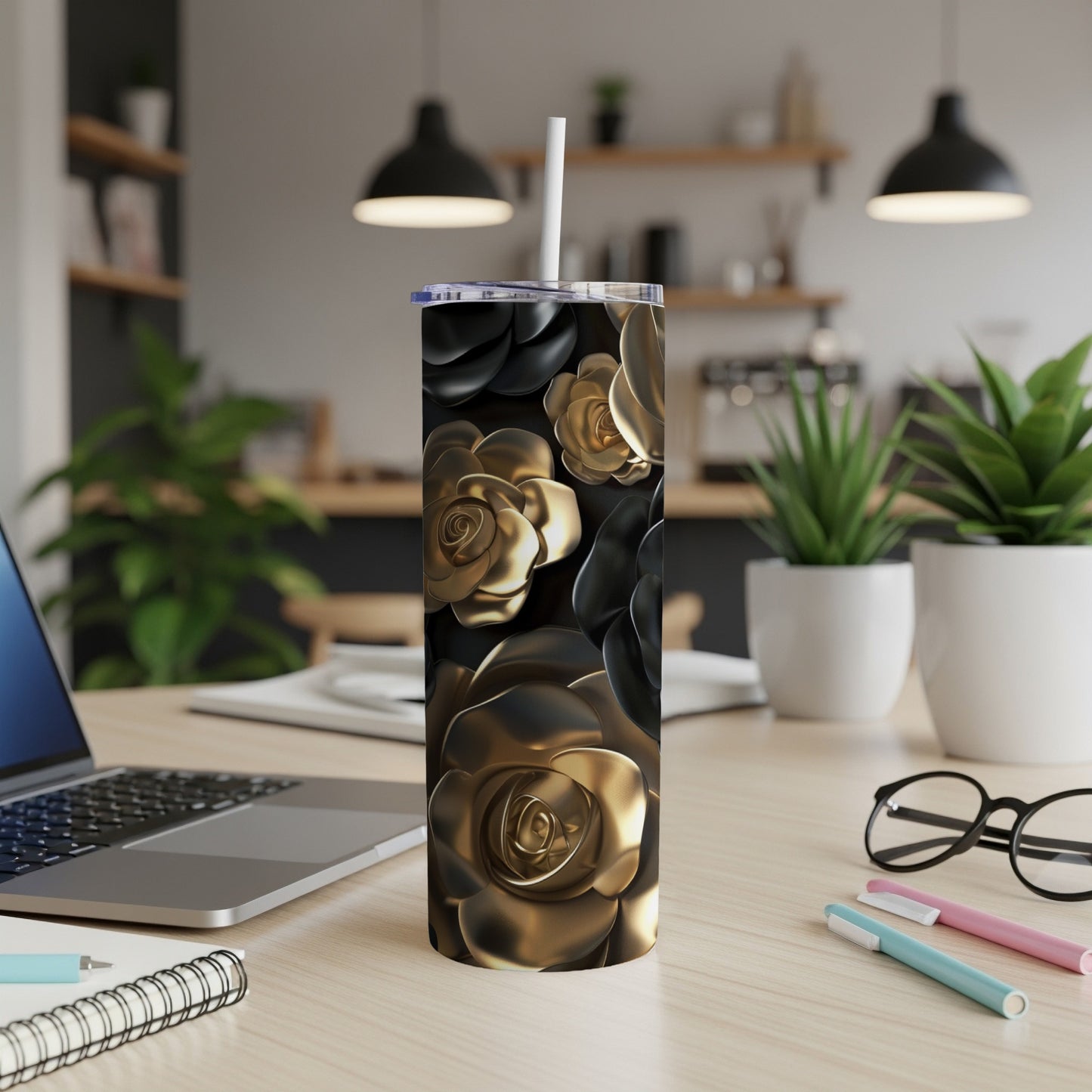 Gold and black rose patterned tumbler with straw on a desk.