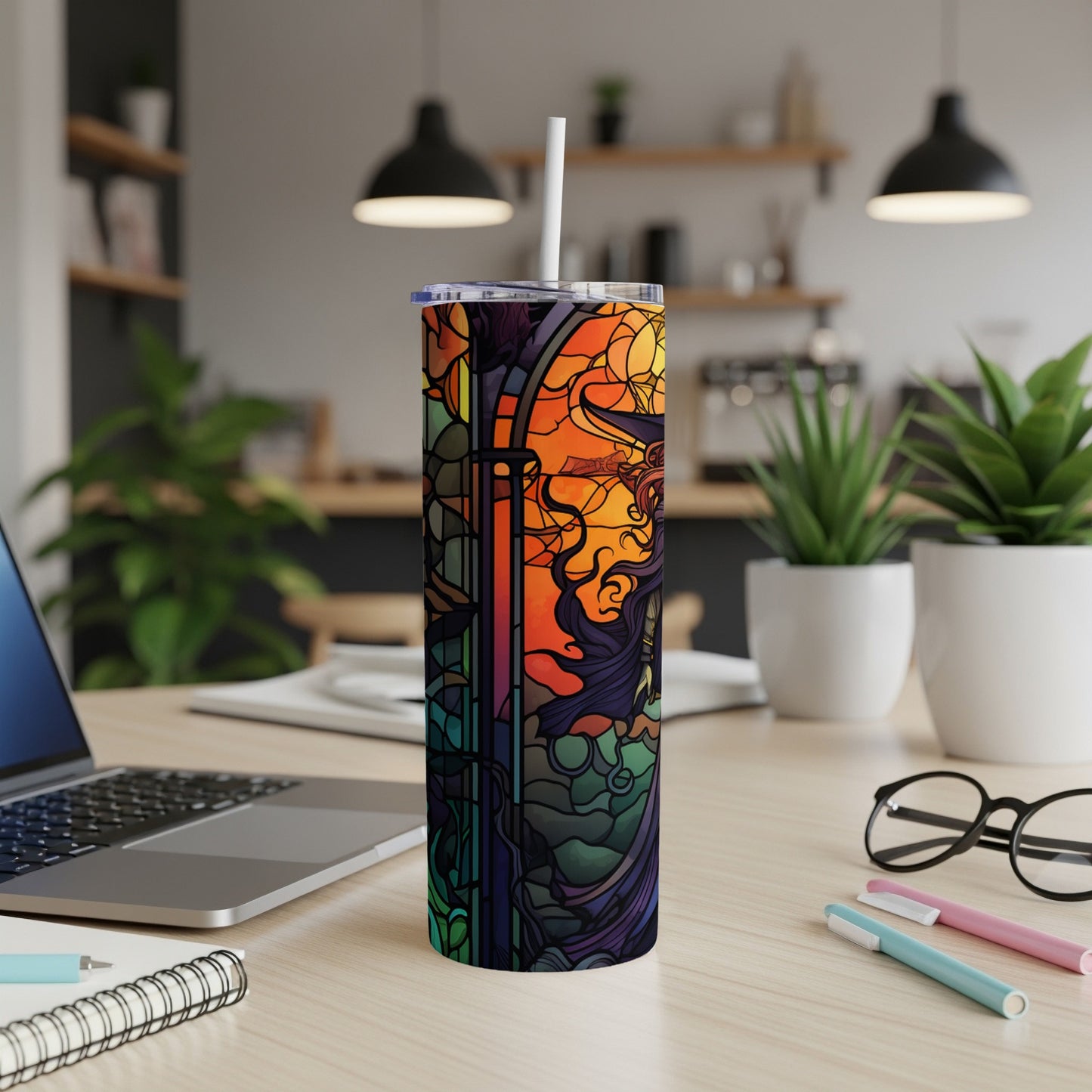 Tall tumbler with stained-glass style witch illustration, on a desk.