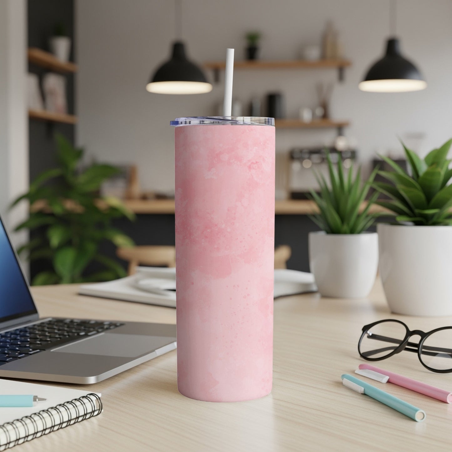 Pink marbled tumbler with straw on a desk with laptop and plants.