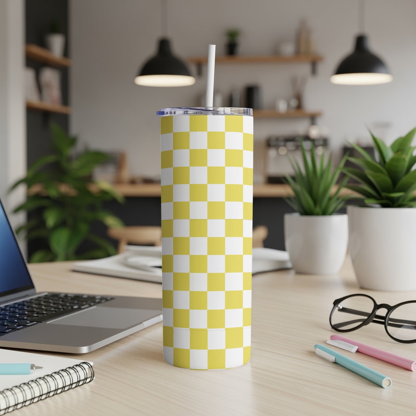 Yellow and white checkered tumbler with straw on a desk.