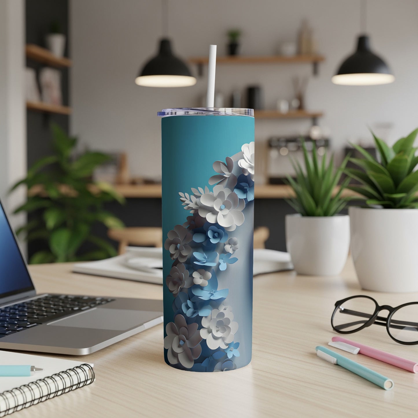 Turquoise tumbler with floral pattern, on a desk with laptop and pens.