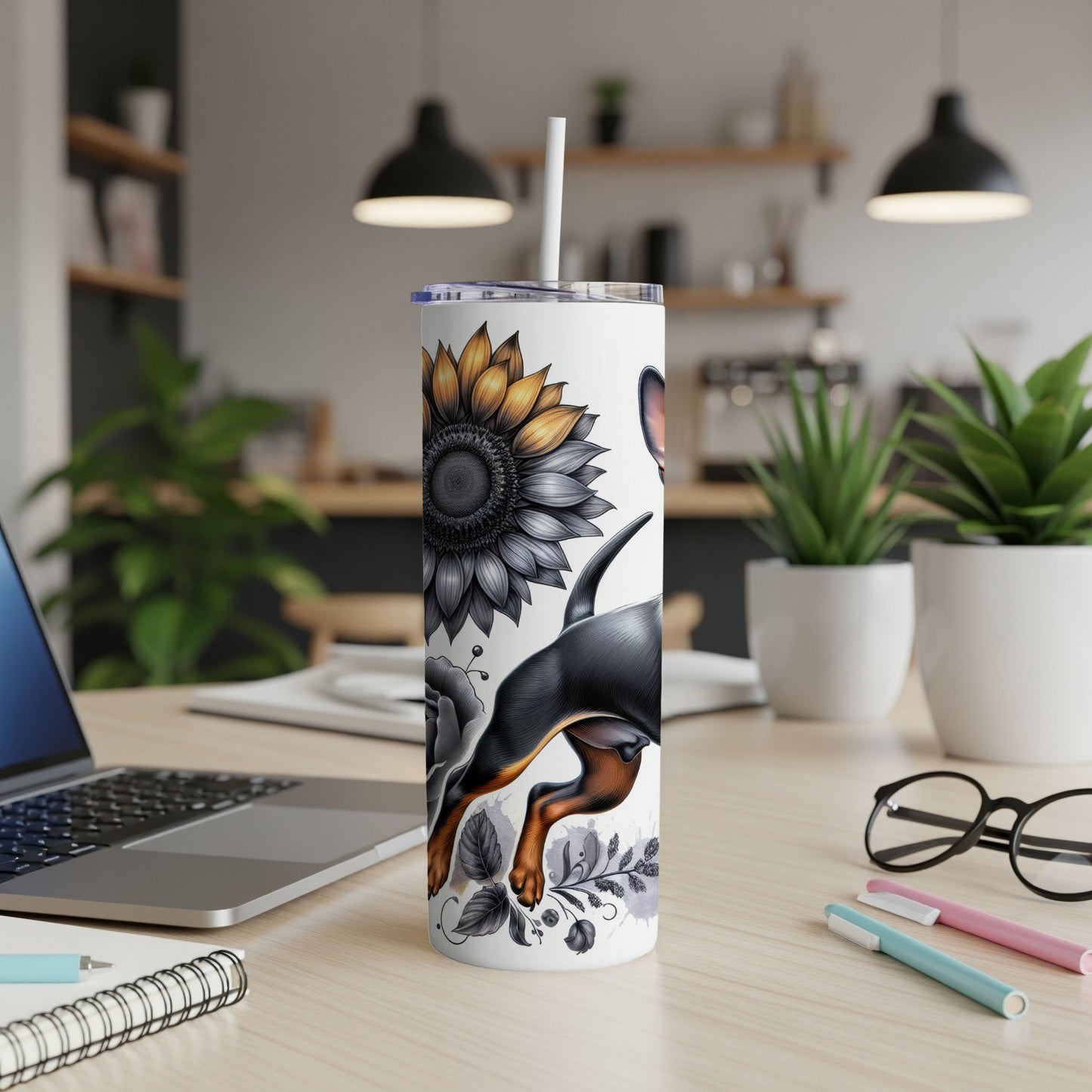 White tumbler with black dog and sunflower illustration on a desk.