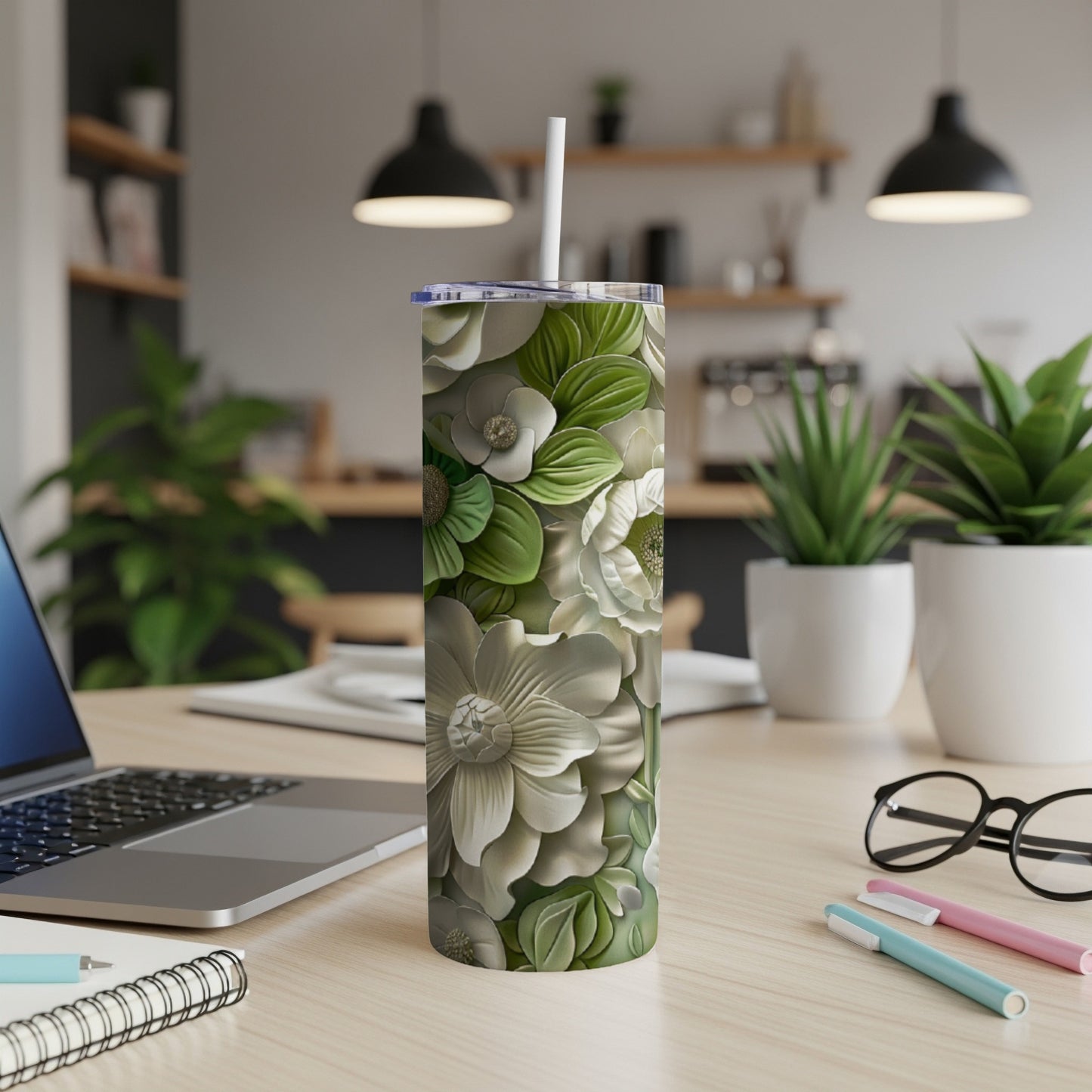 White and green floral tumbler with straw on a desk.