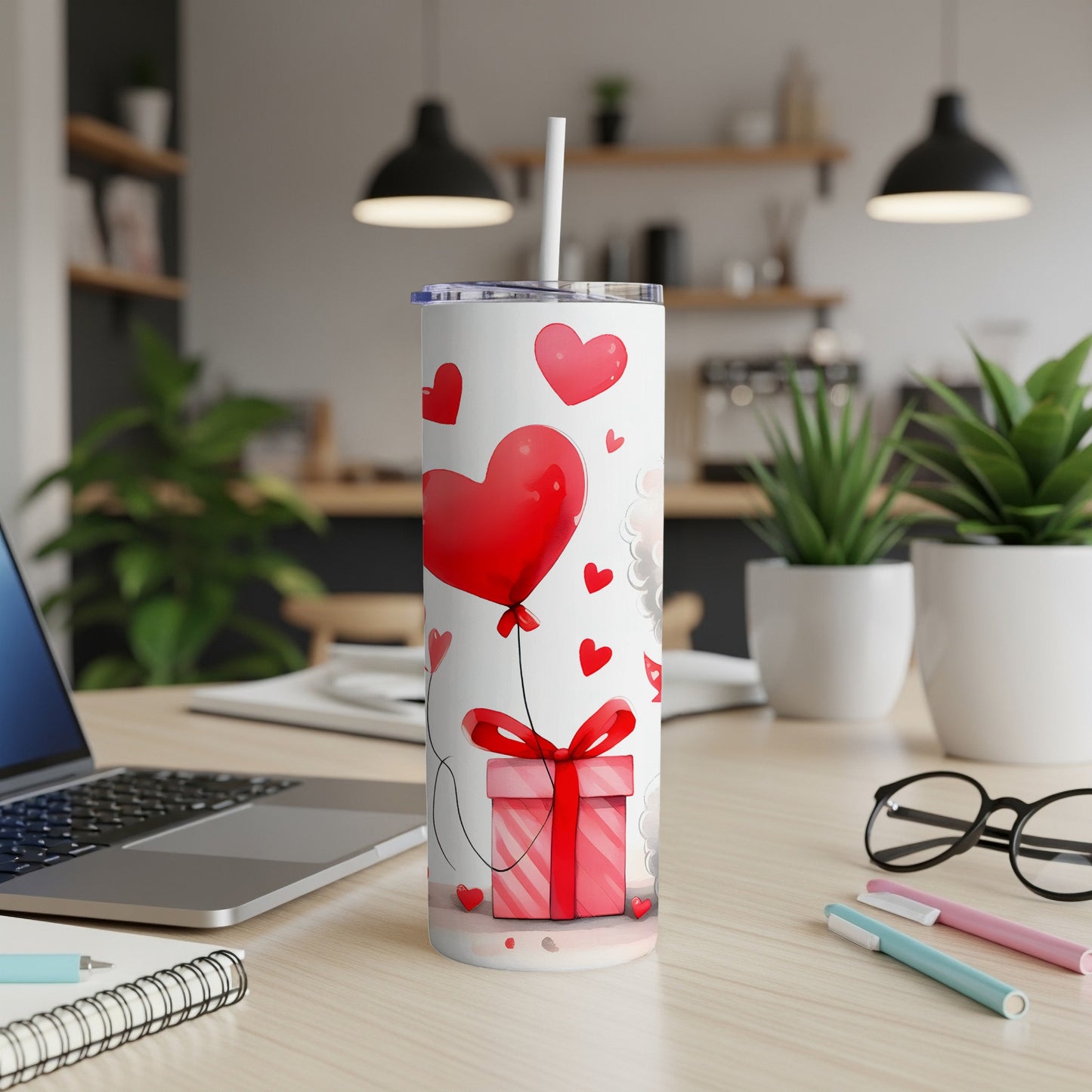 White tumbler with red hearts, gift box, and straw on a desk.