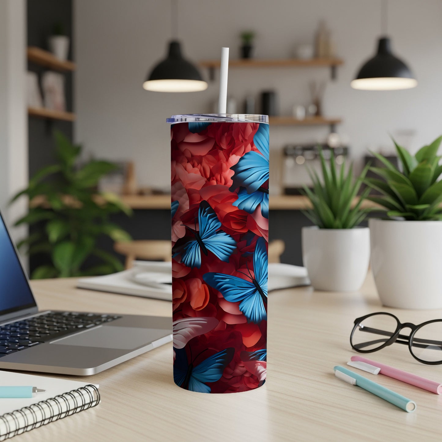 Tall tumbler with blue butterflies and red floral pattern on a desk.