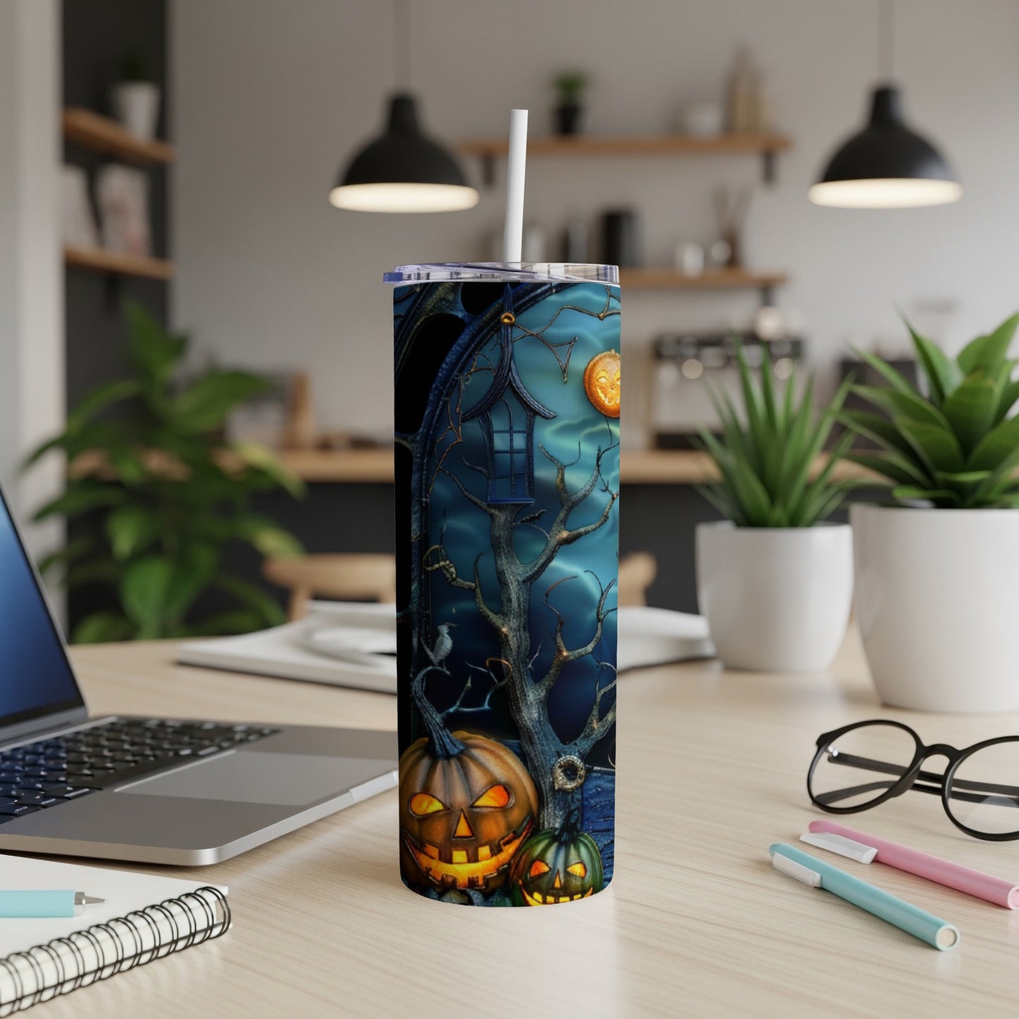 Halloween tumbler with pumpkins, spooky tree, and moon on a desk.