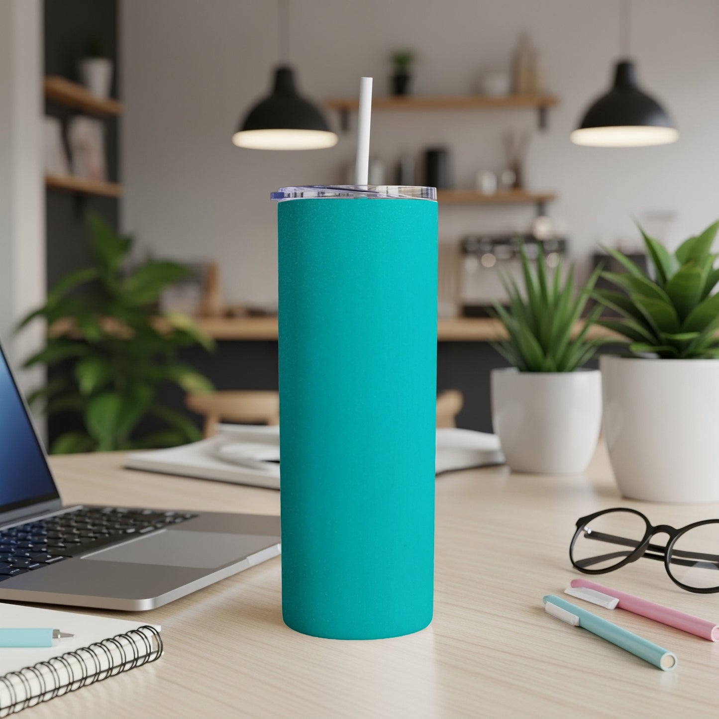 Teal insulated tumbler with white straw on a wooden desk next to a laptop.