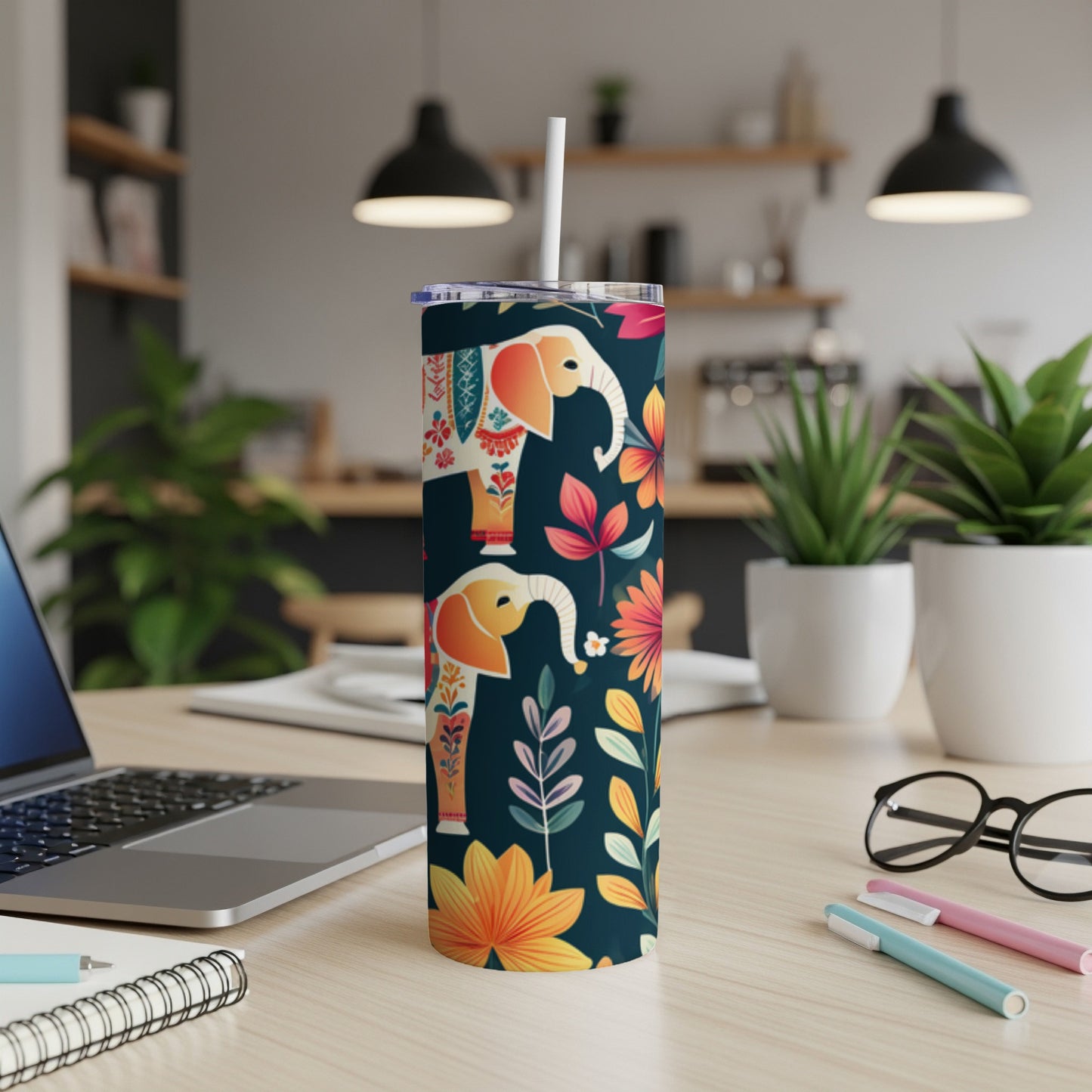 Tall tumbler with elephants and floral pattern, on a desk.