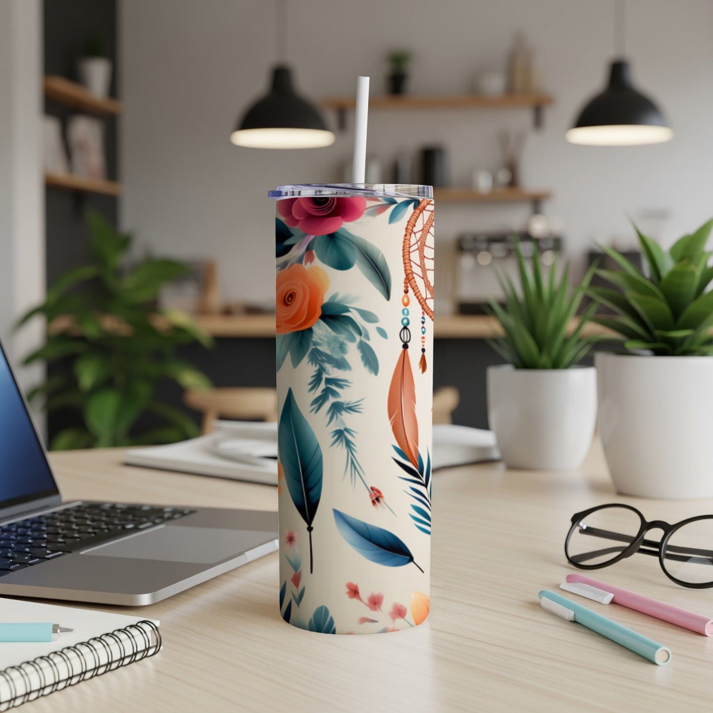 Floral and feather patterned tumbler with a white straw on a desk.