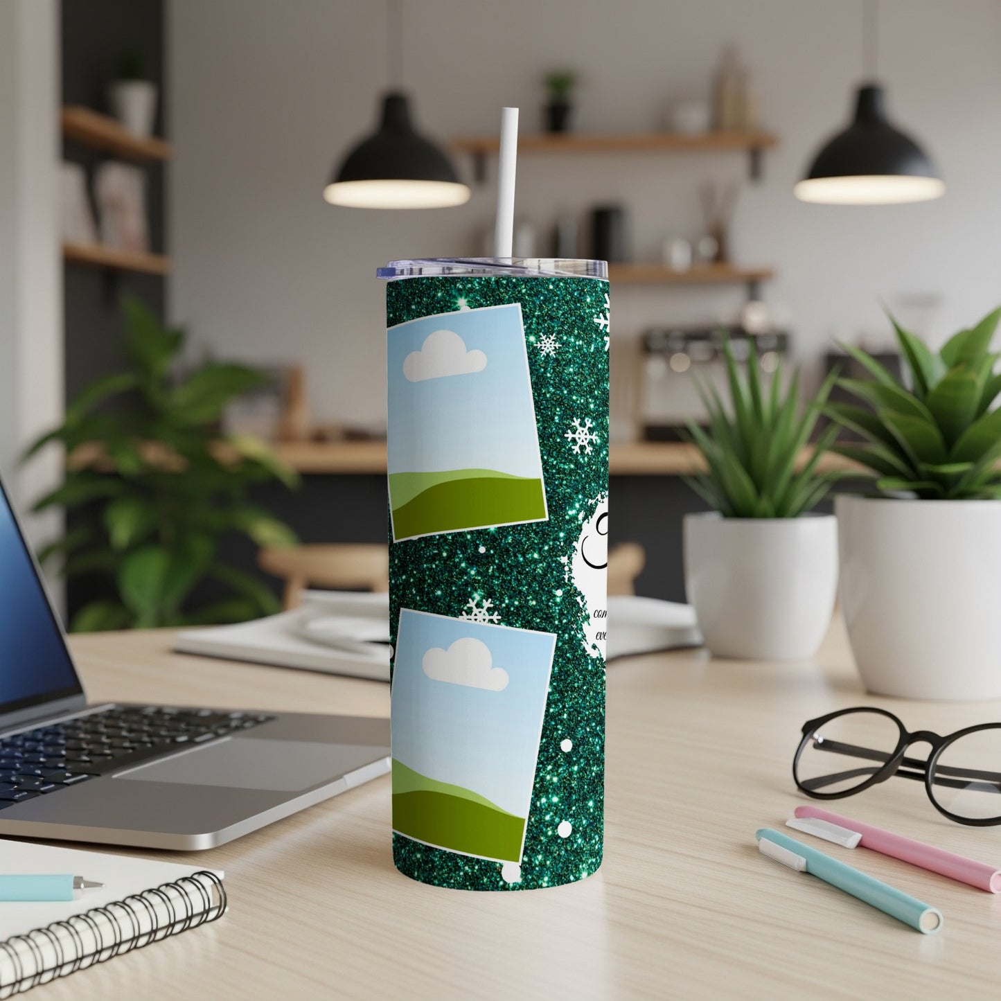 Glittery green tumbler with two photo frames and snowflakes on a desk.