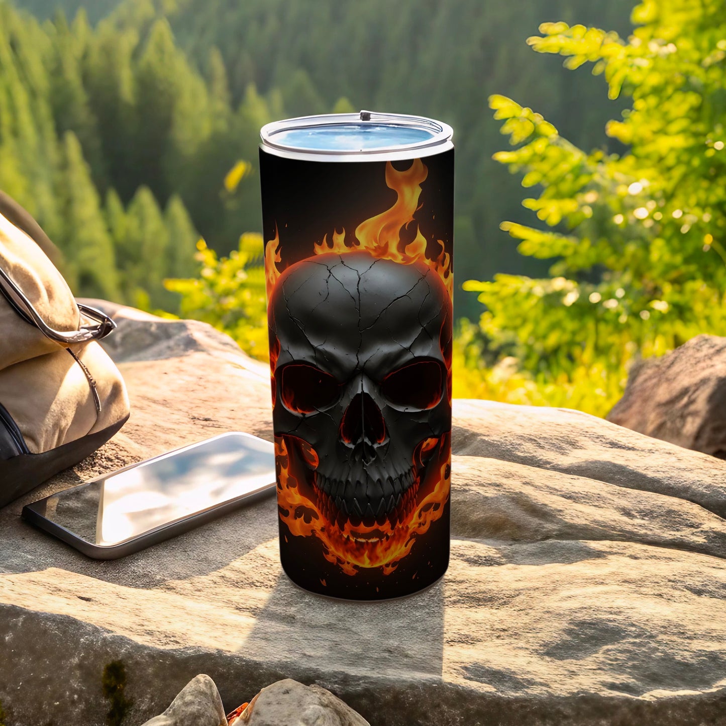 Black skull with flames on a tumbler next to a backpack and phone.