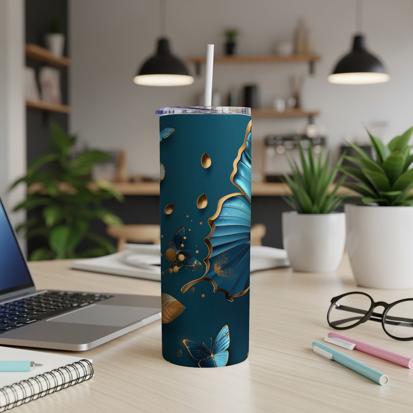Teal tumbler with gold butterfly and floral designs, on a desk.