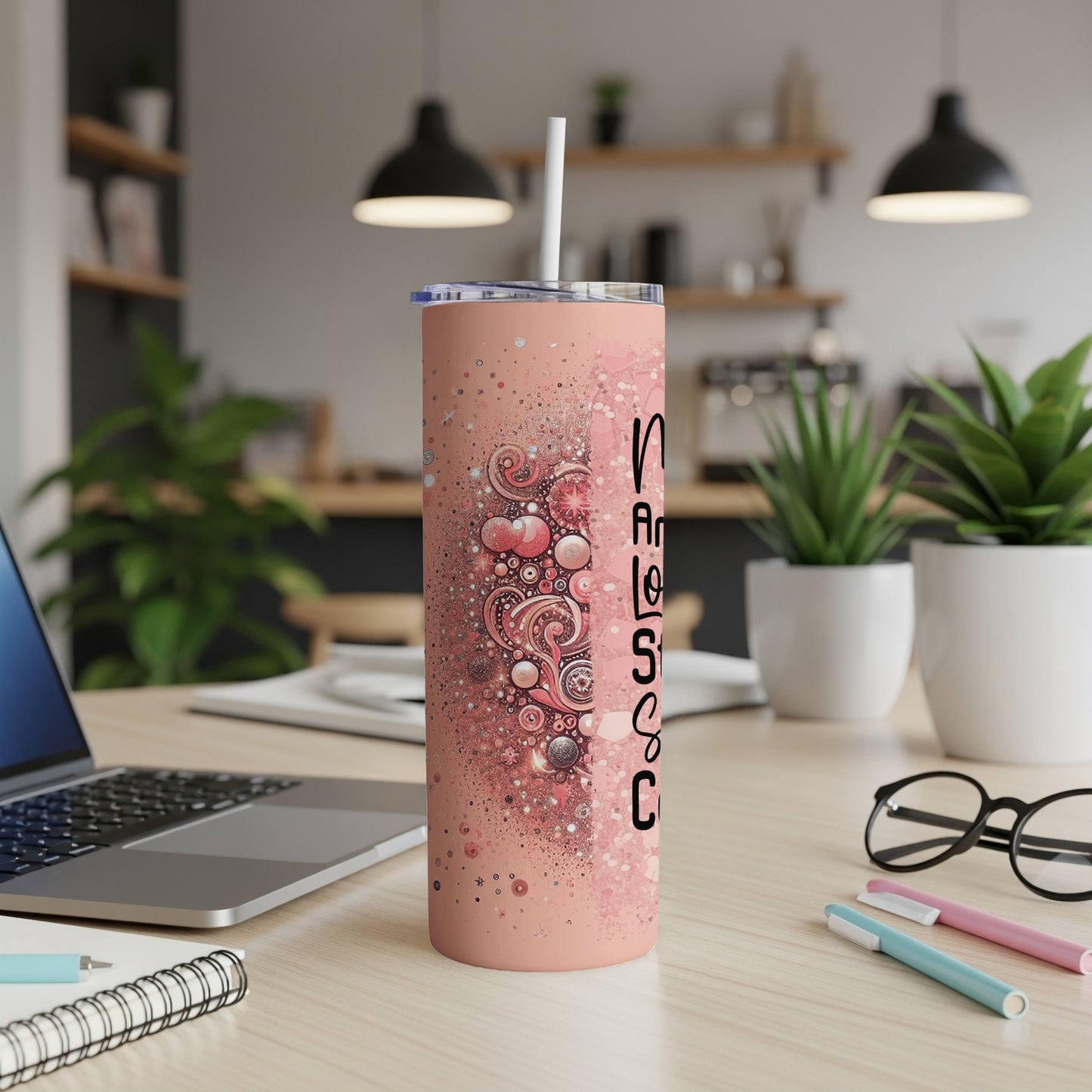 Pink tumbler with white straw on desk, featuring abstract heart and bubble design.