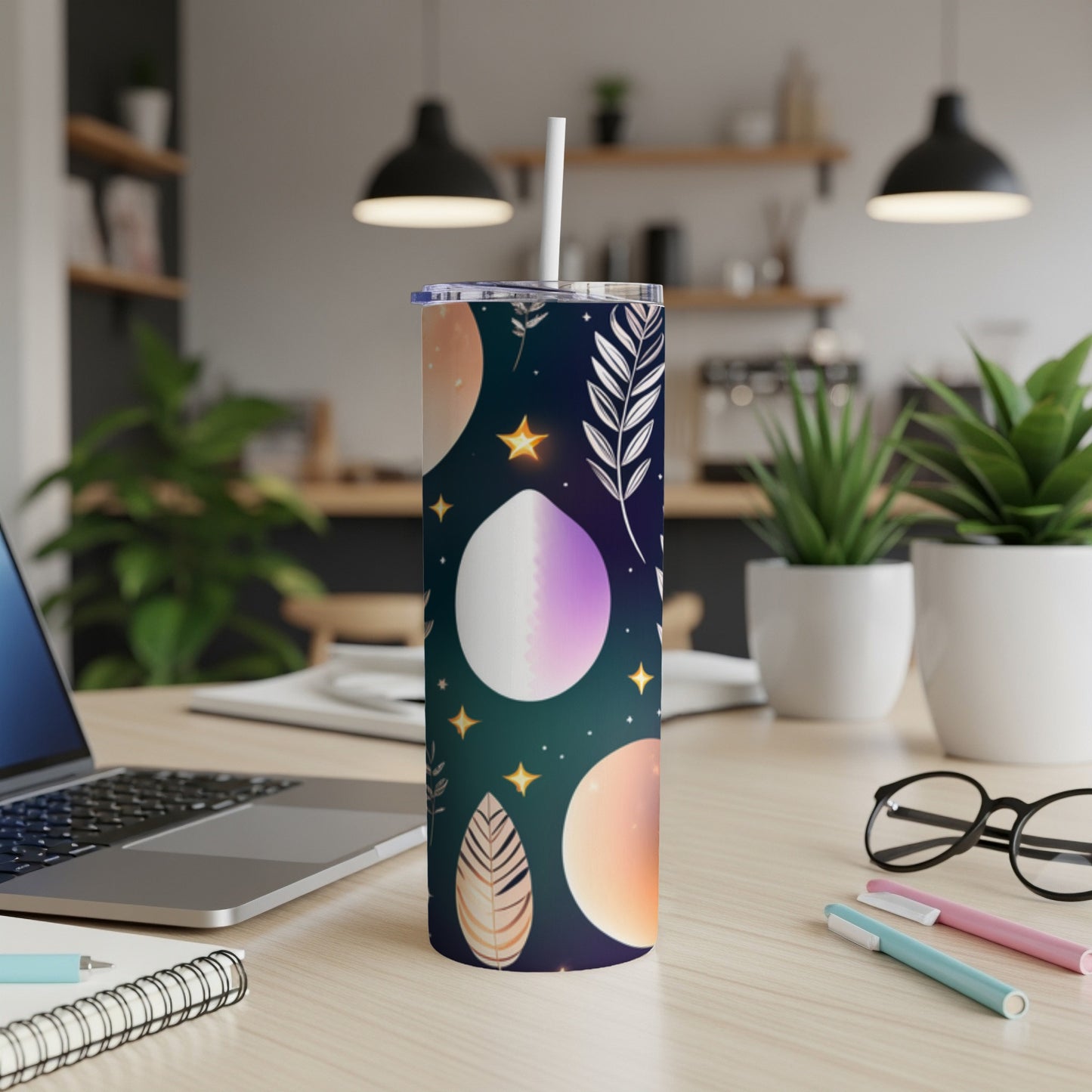 Tall tumbler with celestial print and straw on a desk.