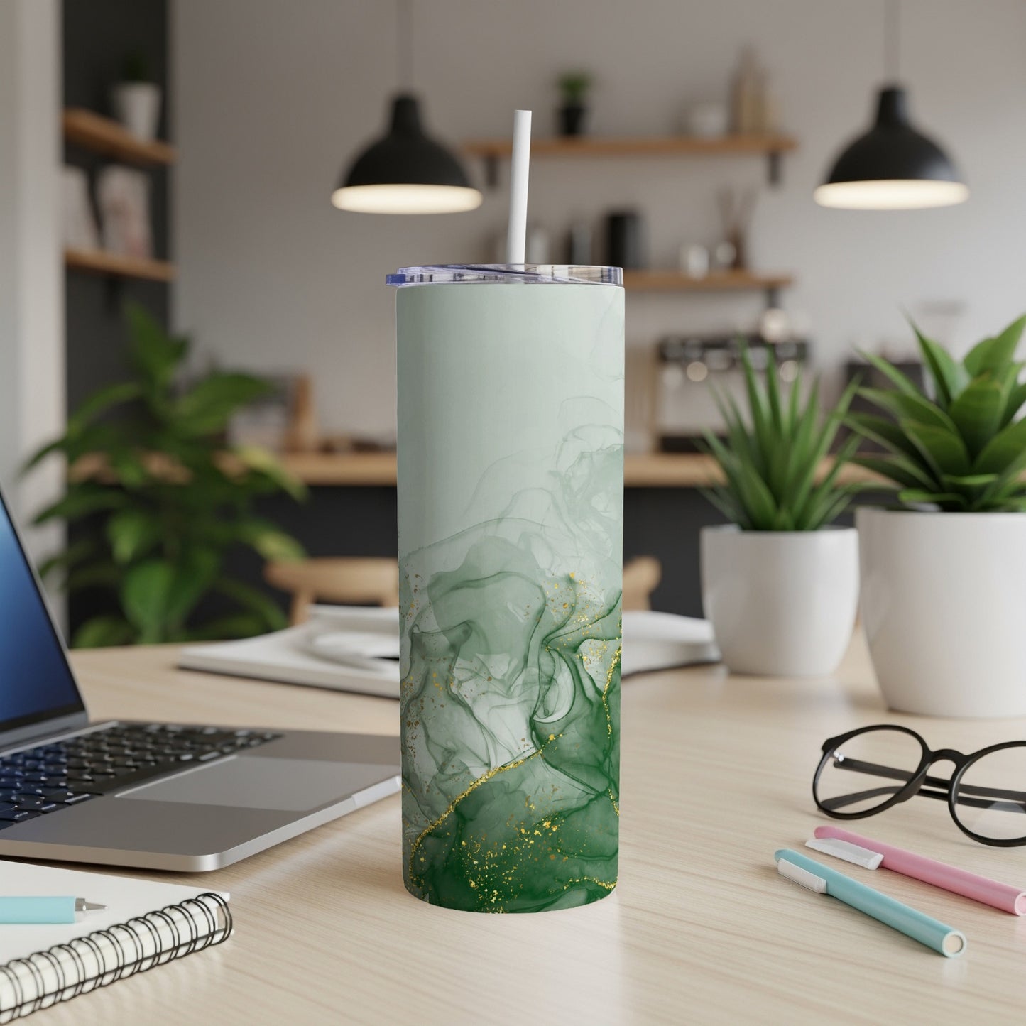 Green abstract marble tumbler with gold accents and straw on a desk.
