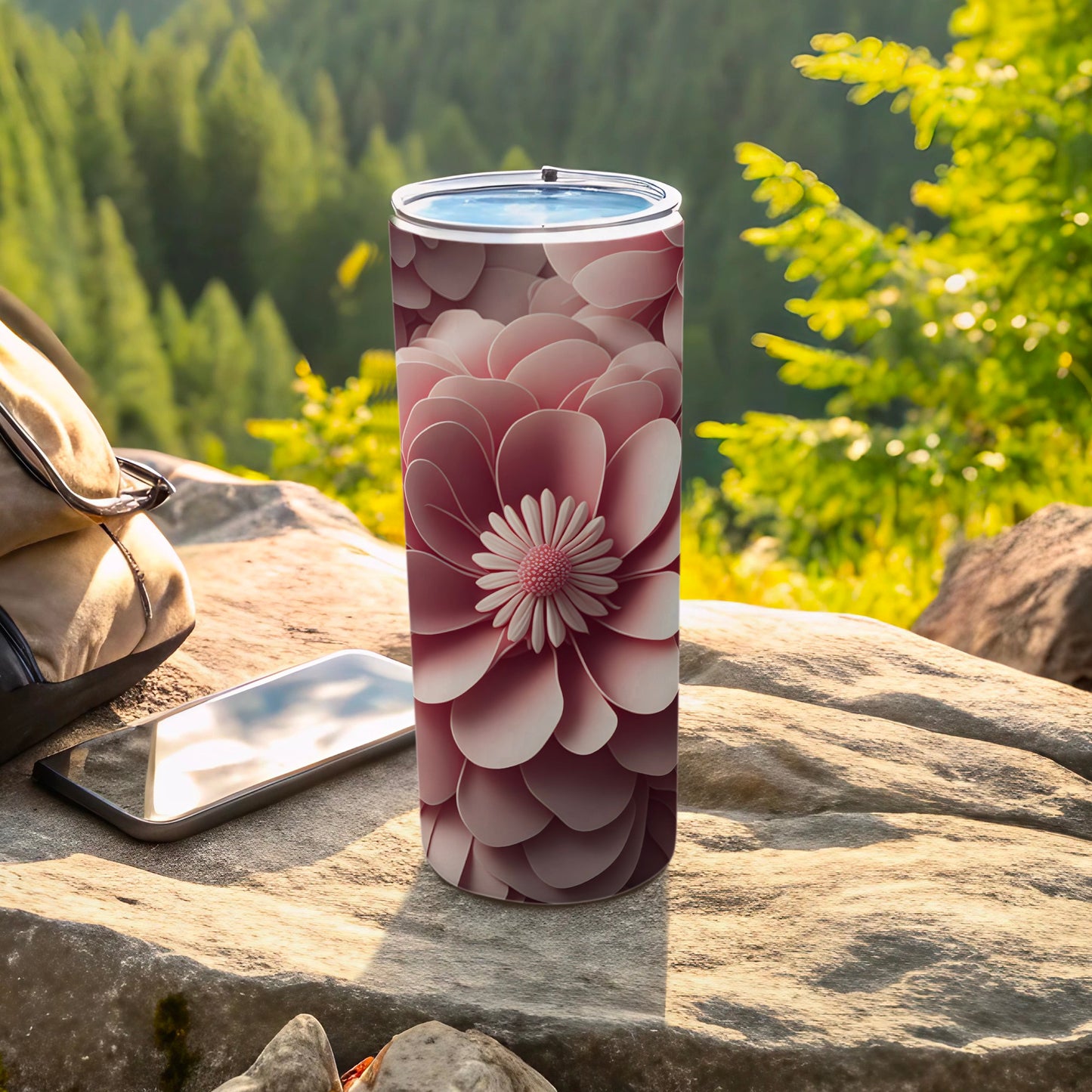 Pink floral pattern tumbler on rocky surface with phone and backpack.