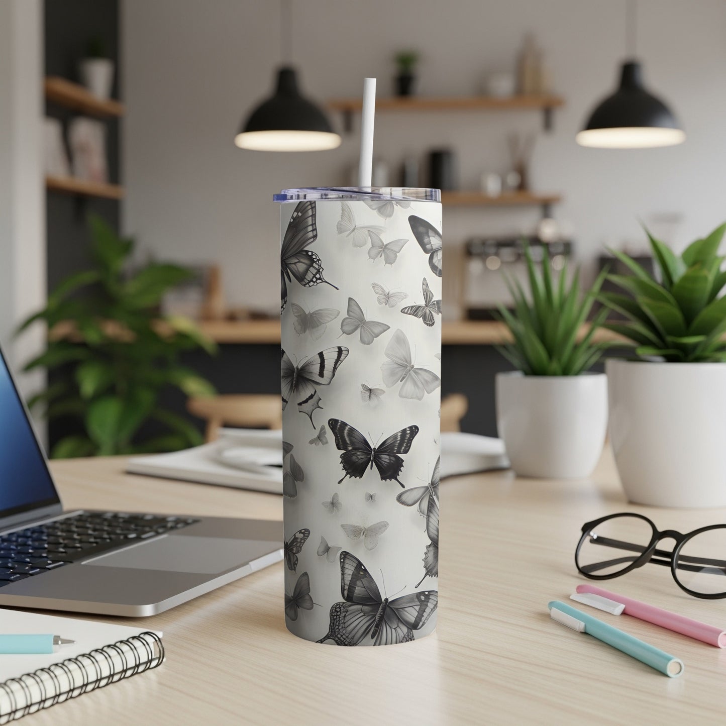 Silver tumbler with a repeating butterfly pattern on a desk.