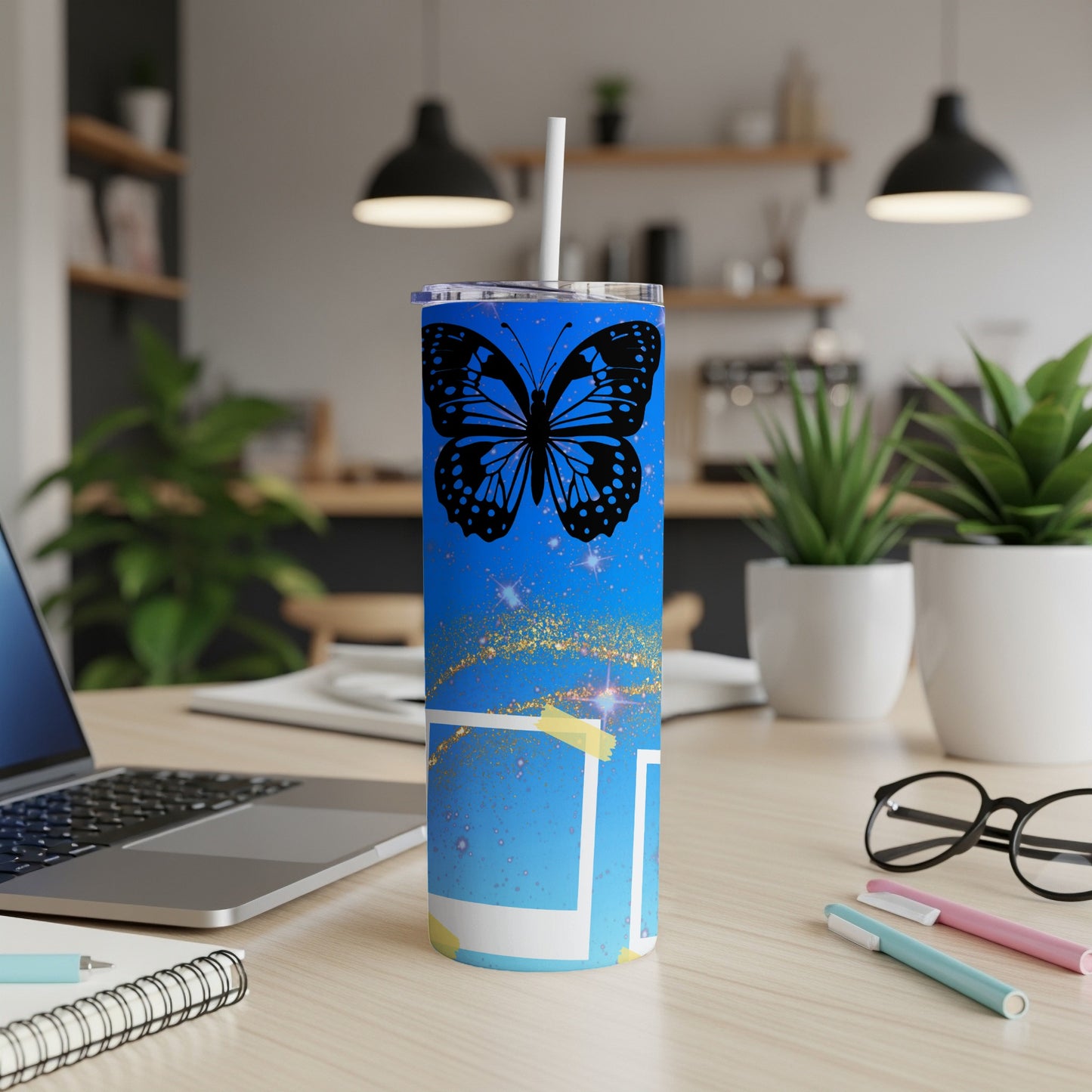 Blue tumbler with black butterfly design, straw, and sparkly accents on a desk.