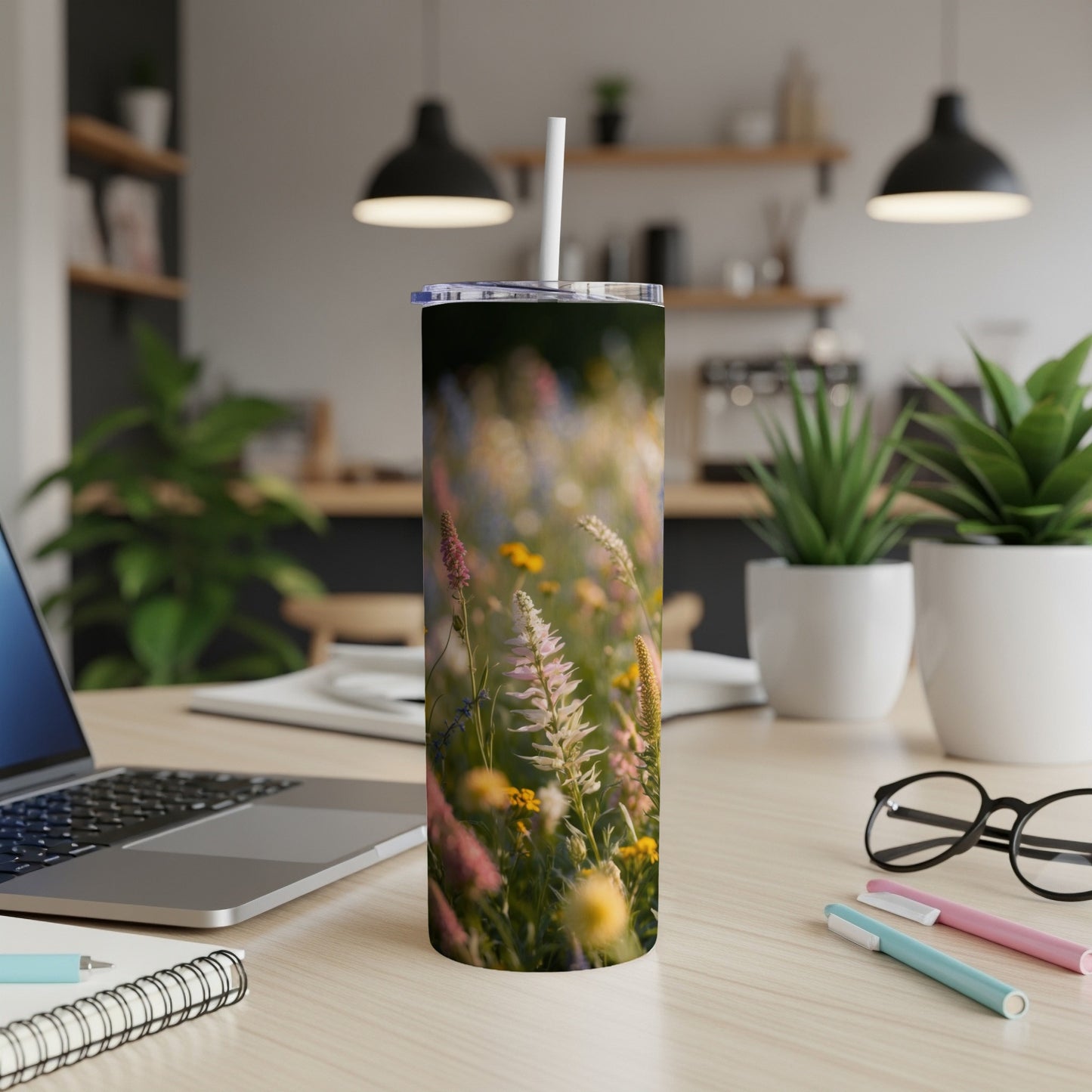 Tall tumbler with a floral meadow design, on a desk with laptop.