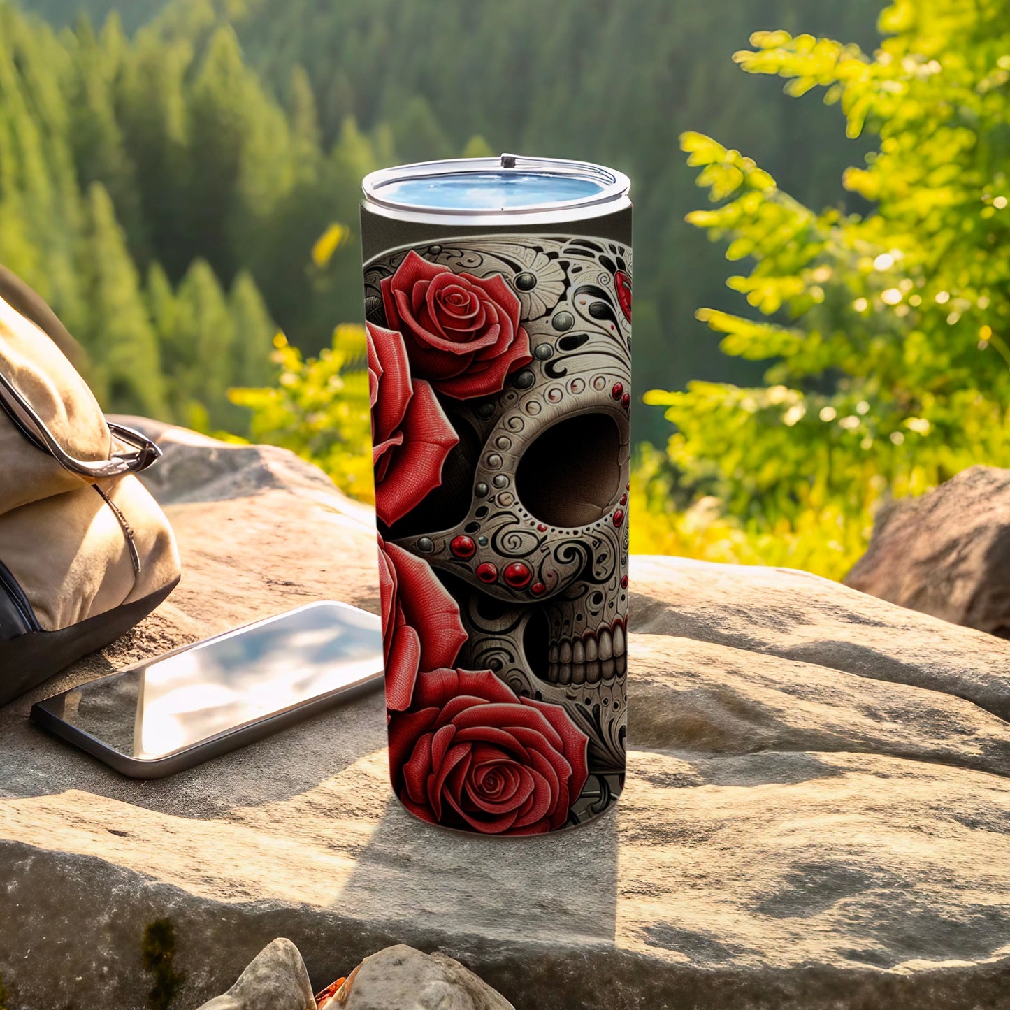 Tall tumbler with red roses and a skull design, on a rock.
