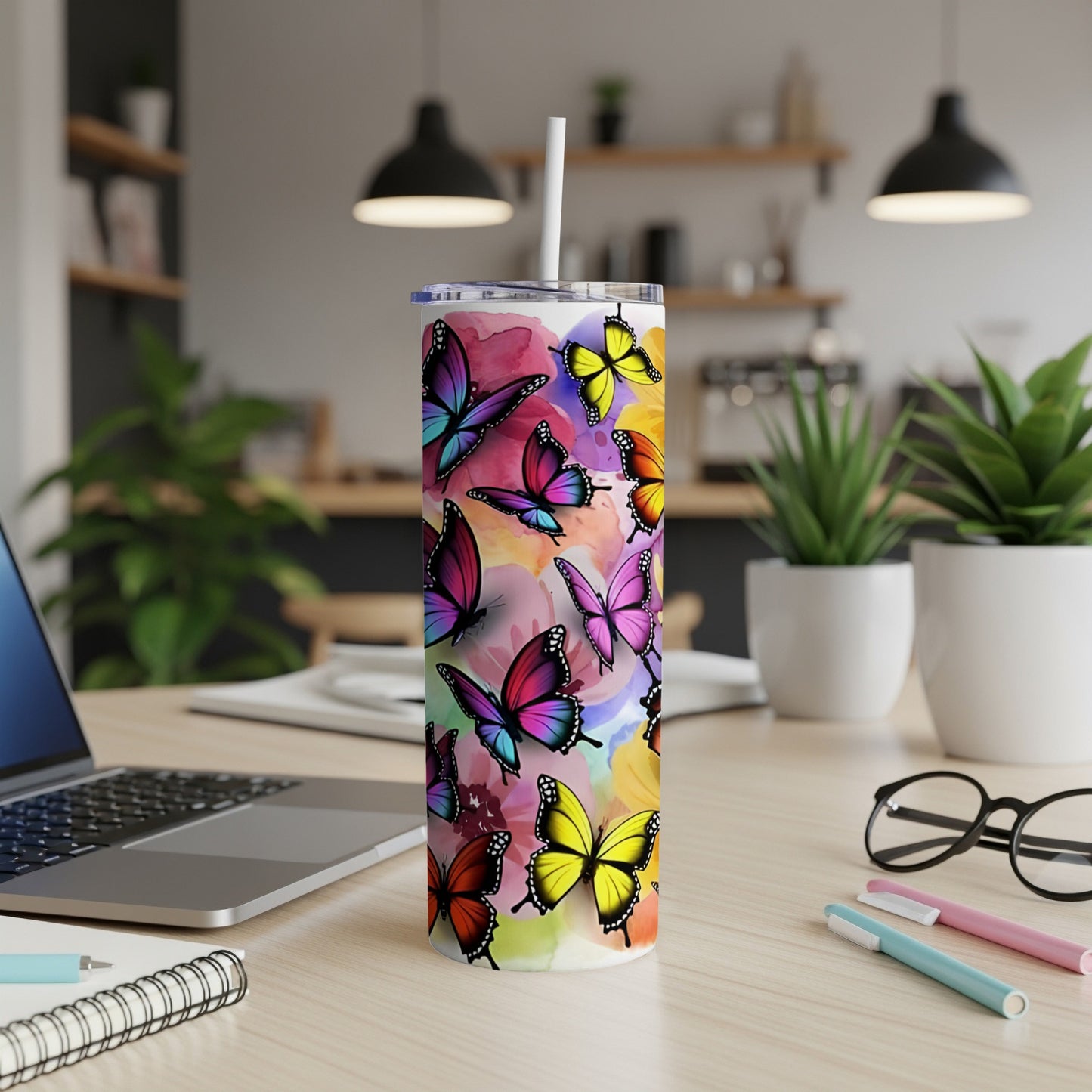 Colorful butterflies adorn a white tumbler on a desk with a laptop and supplies.