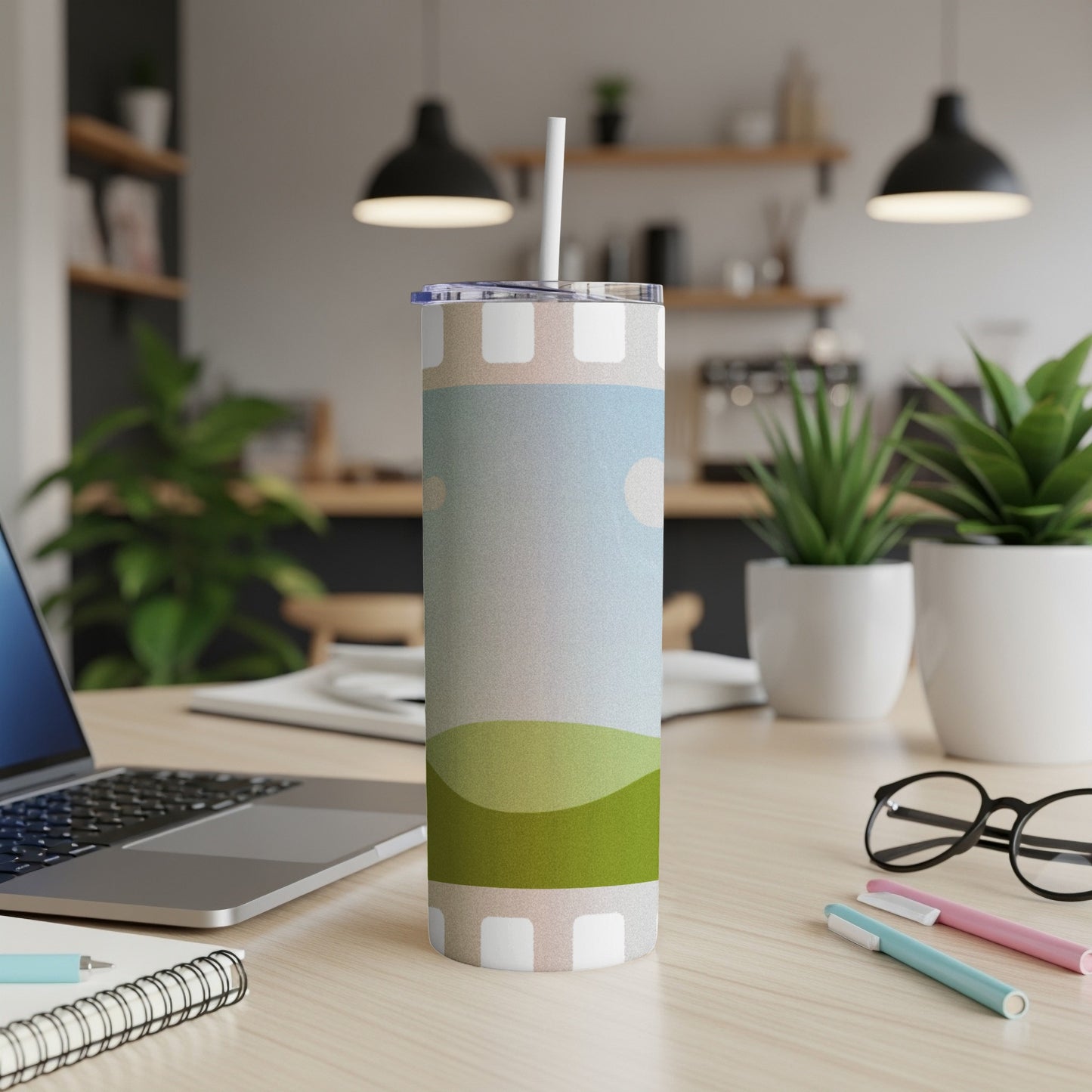 Tumbler with abstract landscape design featuring hills and sky on a desk.