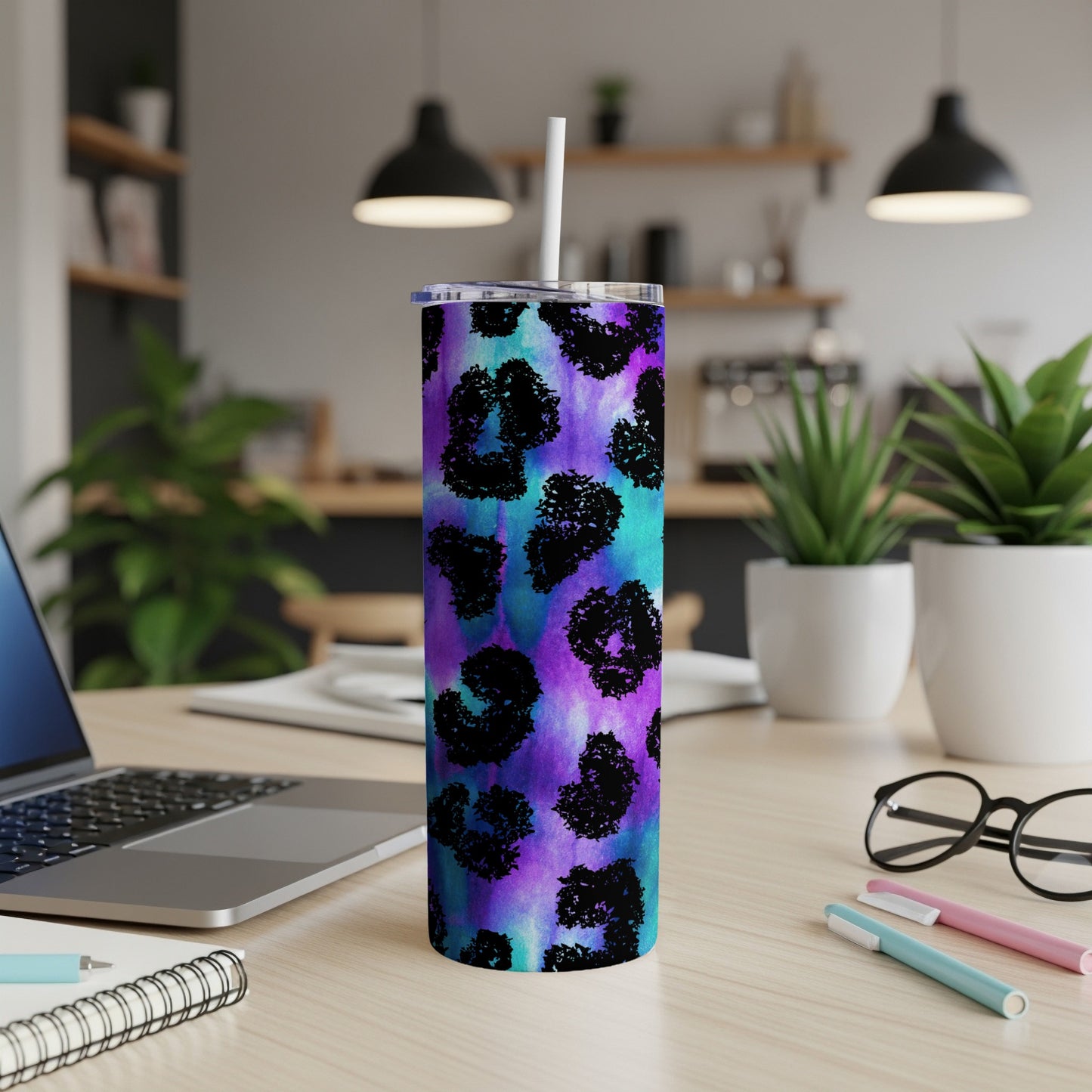 Leopard print tumbler with a straw on a wooden desk next to a laptop.