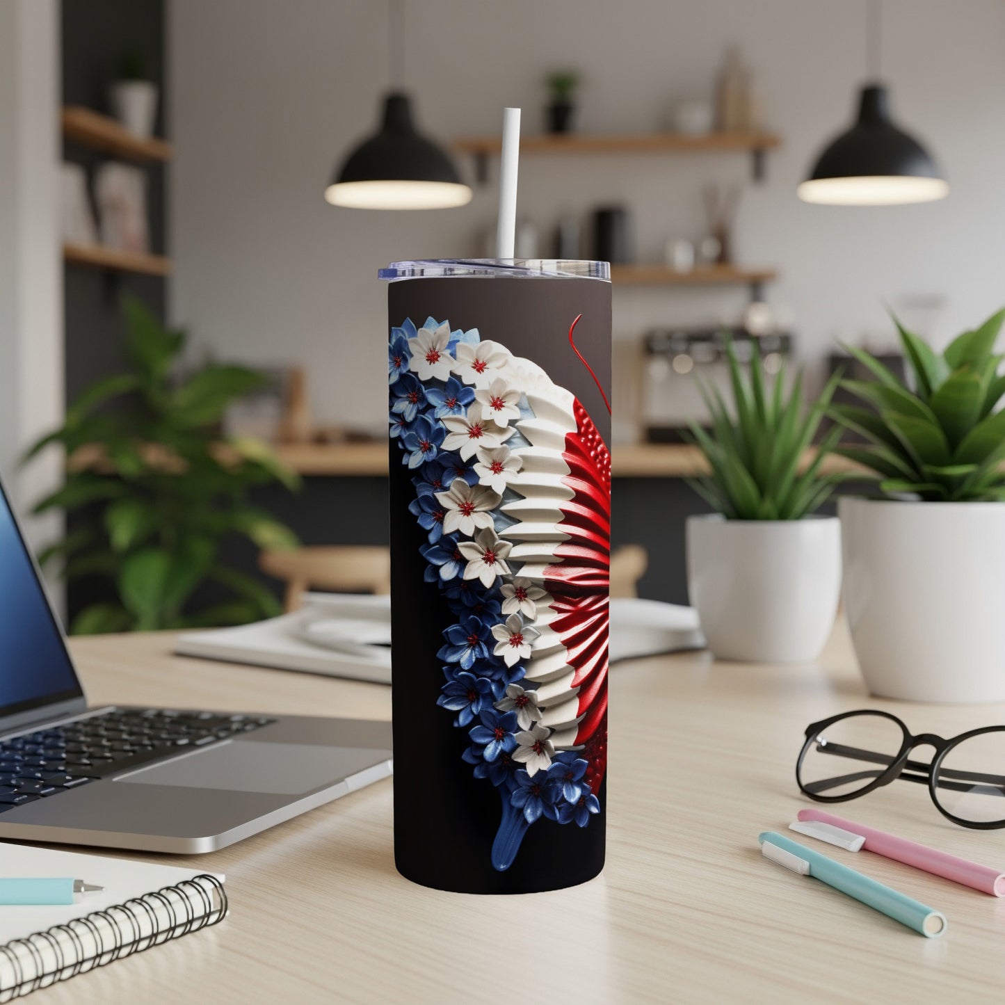 Black tumbler with red, white, and blue floral design, on a desk with laptop and pens.