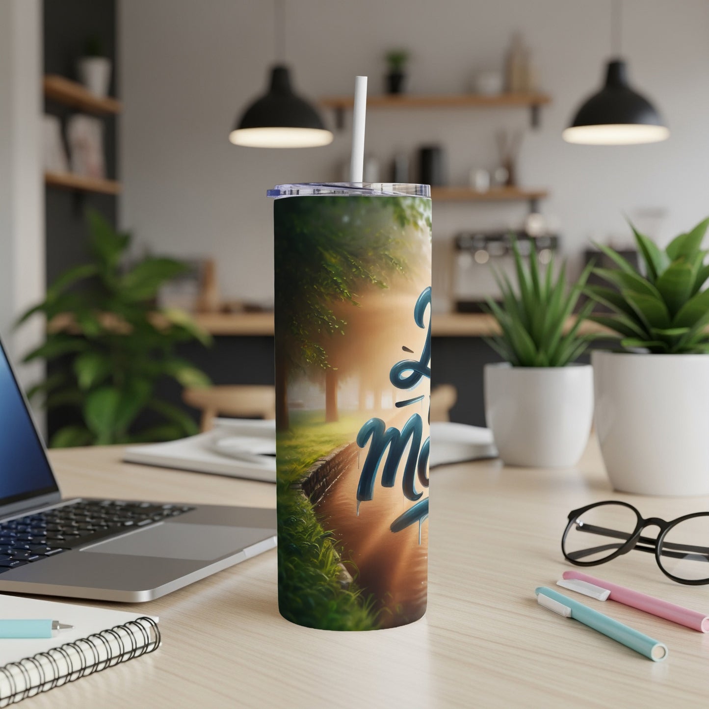 "Love More" tumbler with a serene nature scene and sunlight.