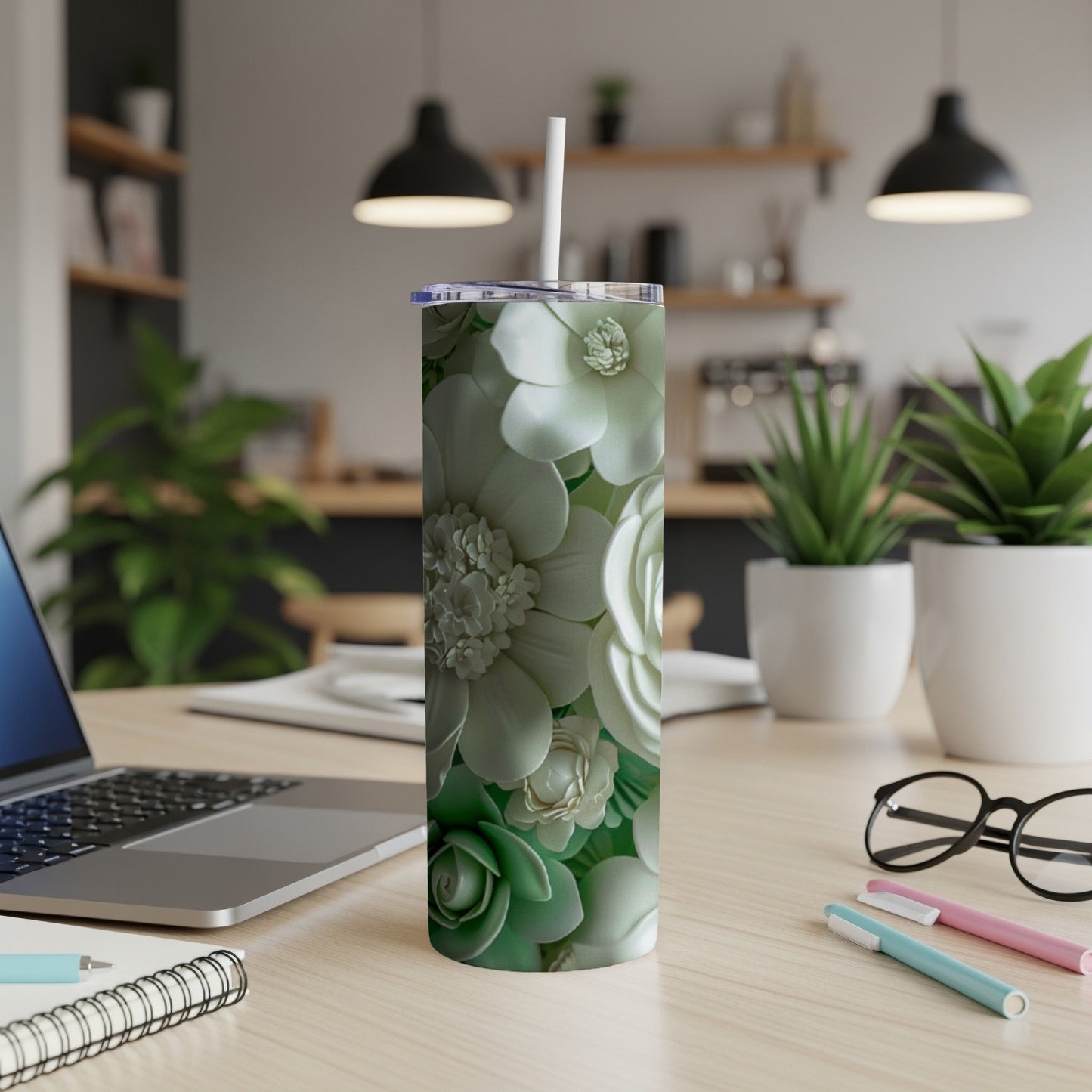 Floral patterned tumbler with straw on a desk with a laptop and pens.