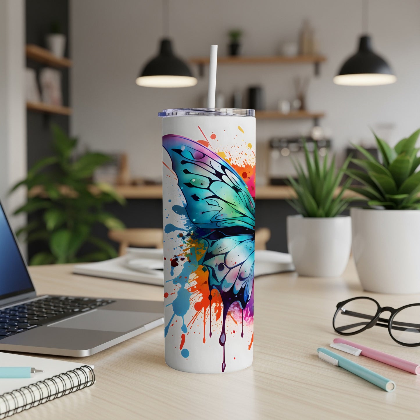 White tumbler with a colorful butterfly wing splatter design and straw.