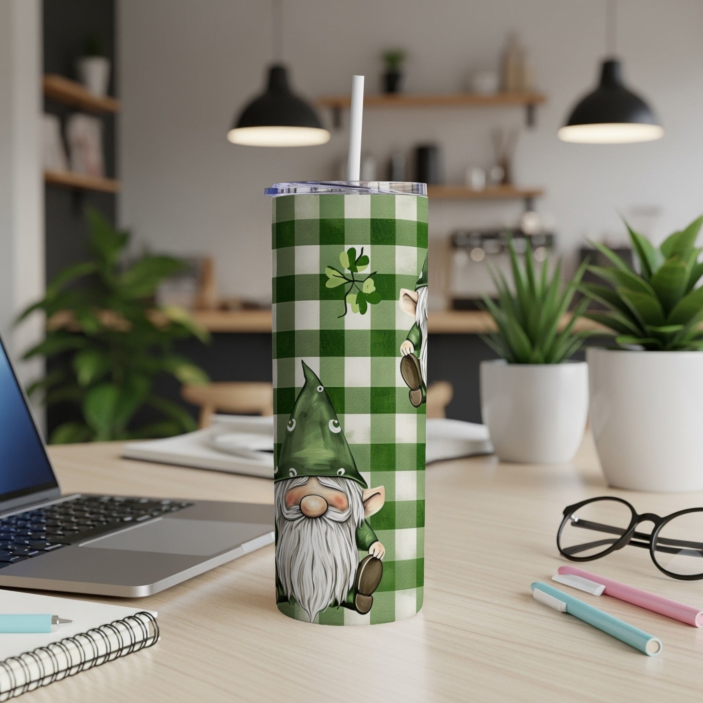 Green and white plaid tumbler with gnome design and straw on desk.