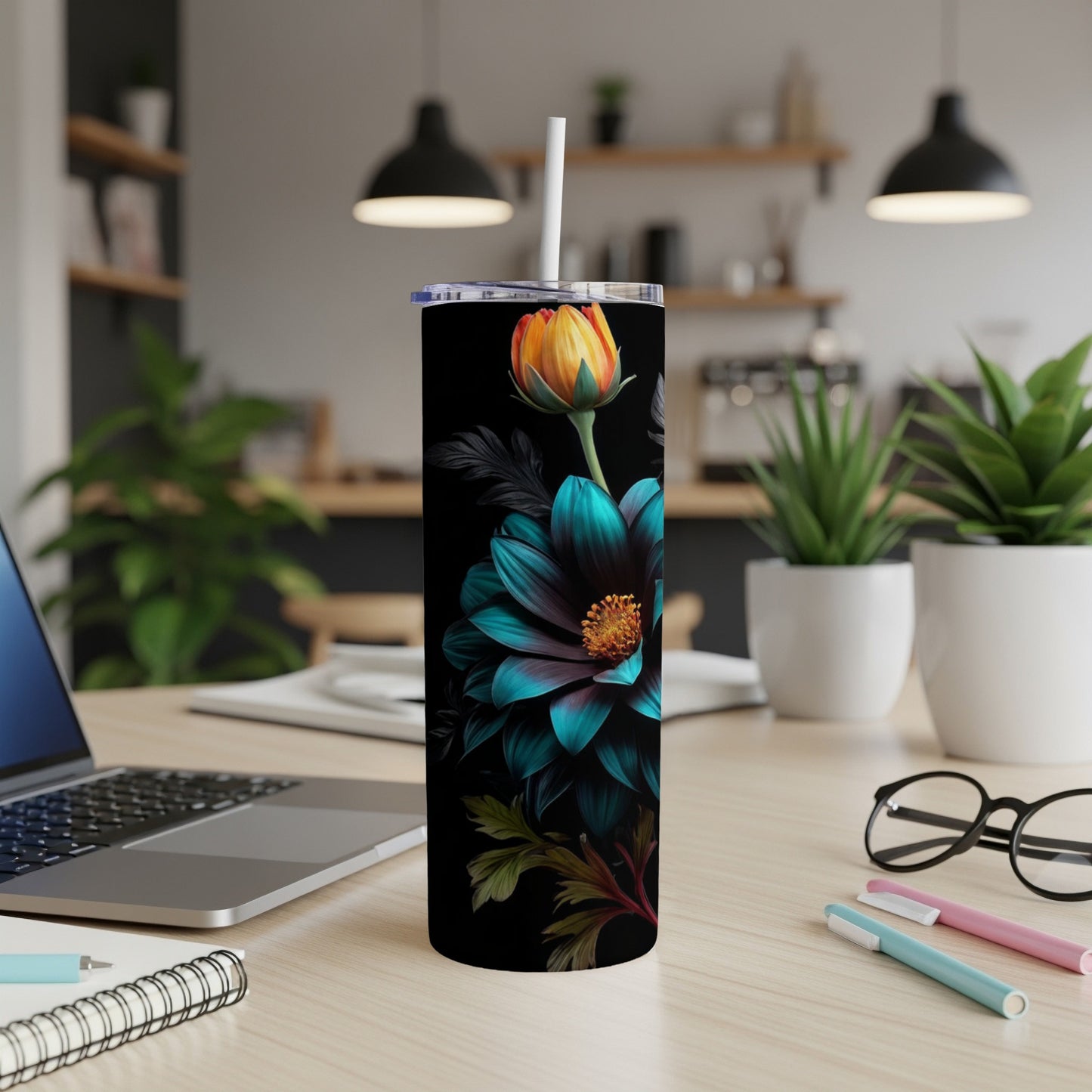 Black tumbler with teal flower and orange center, on a desk.