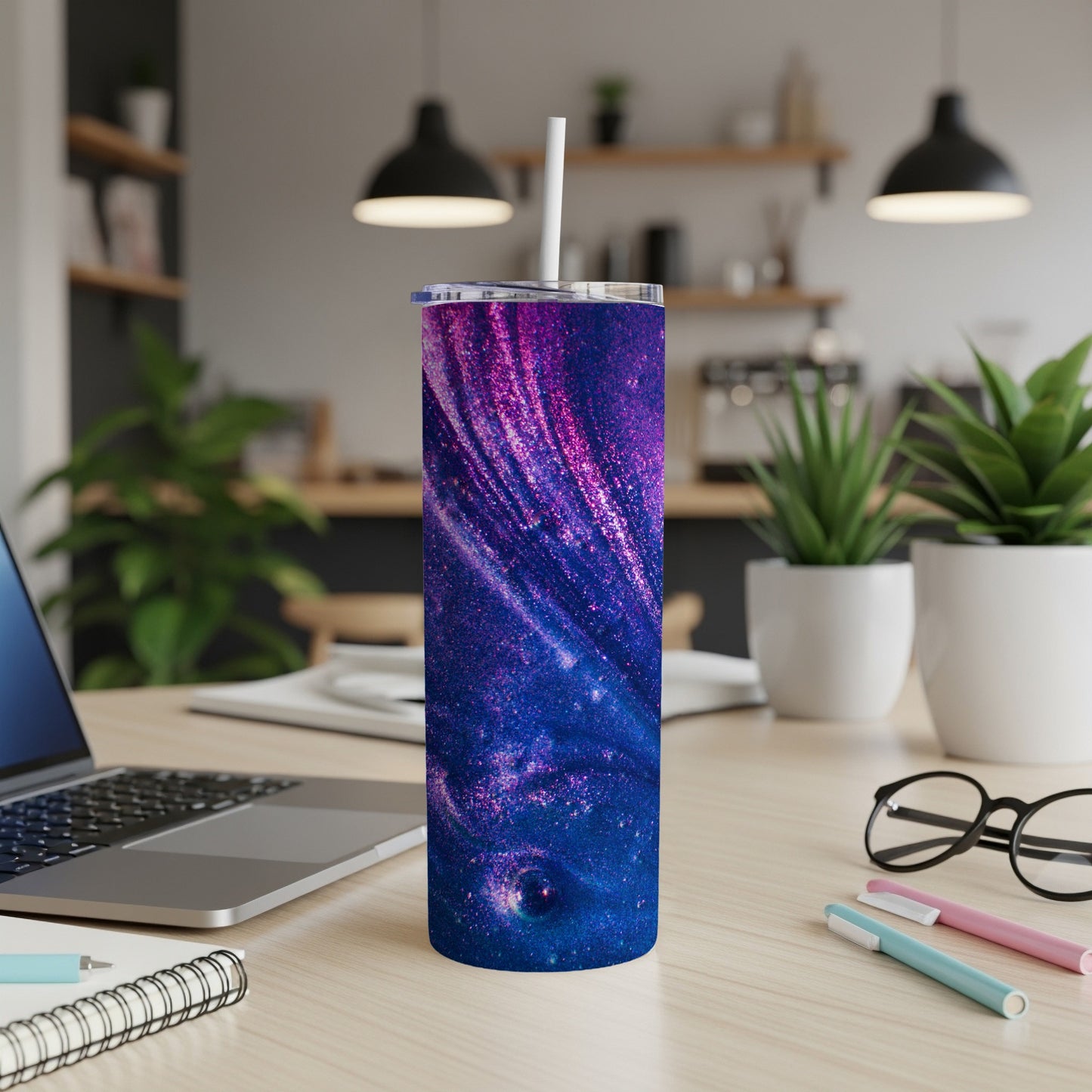 Purple and blue glitter galaxy tumbler with white straw on a desk.
