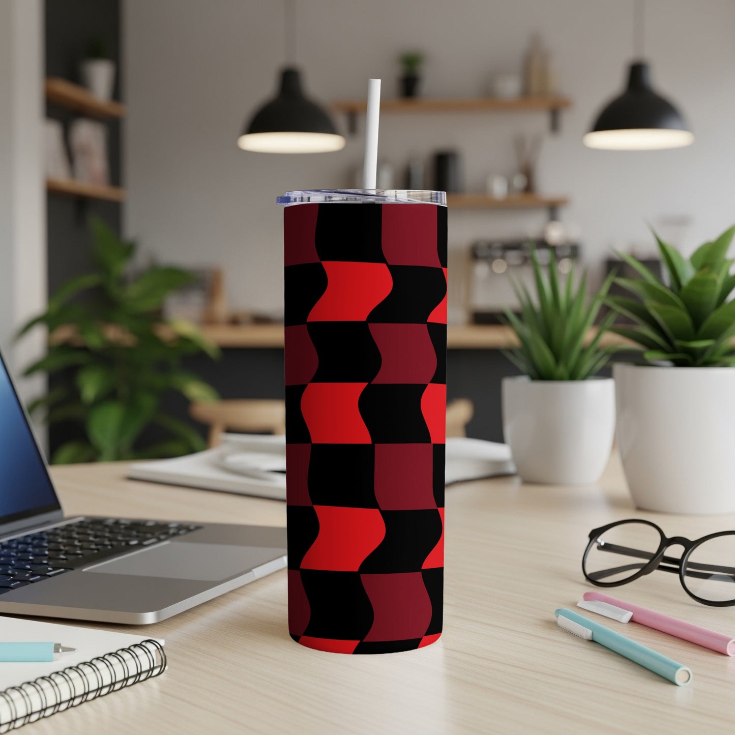 Red and black checkered tumbler with straw on a desk.