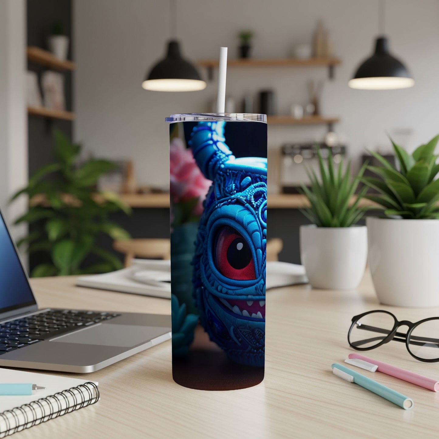 Blue monster tumbler with red eye on a desk next to a laptop.