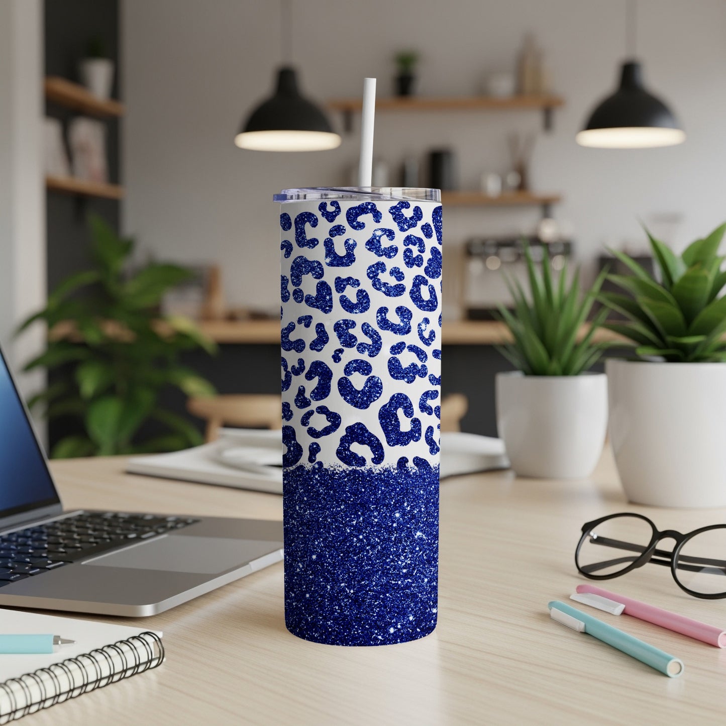 Blue glitter tumbler with white leopard print design on wooden desk.