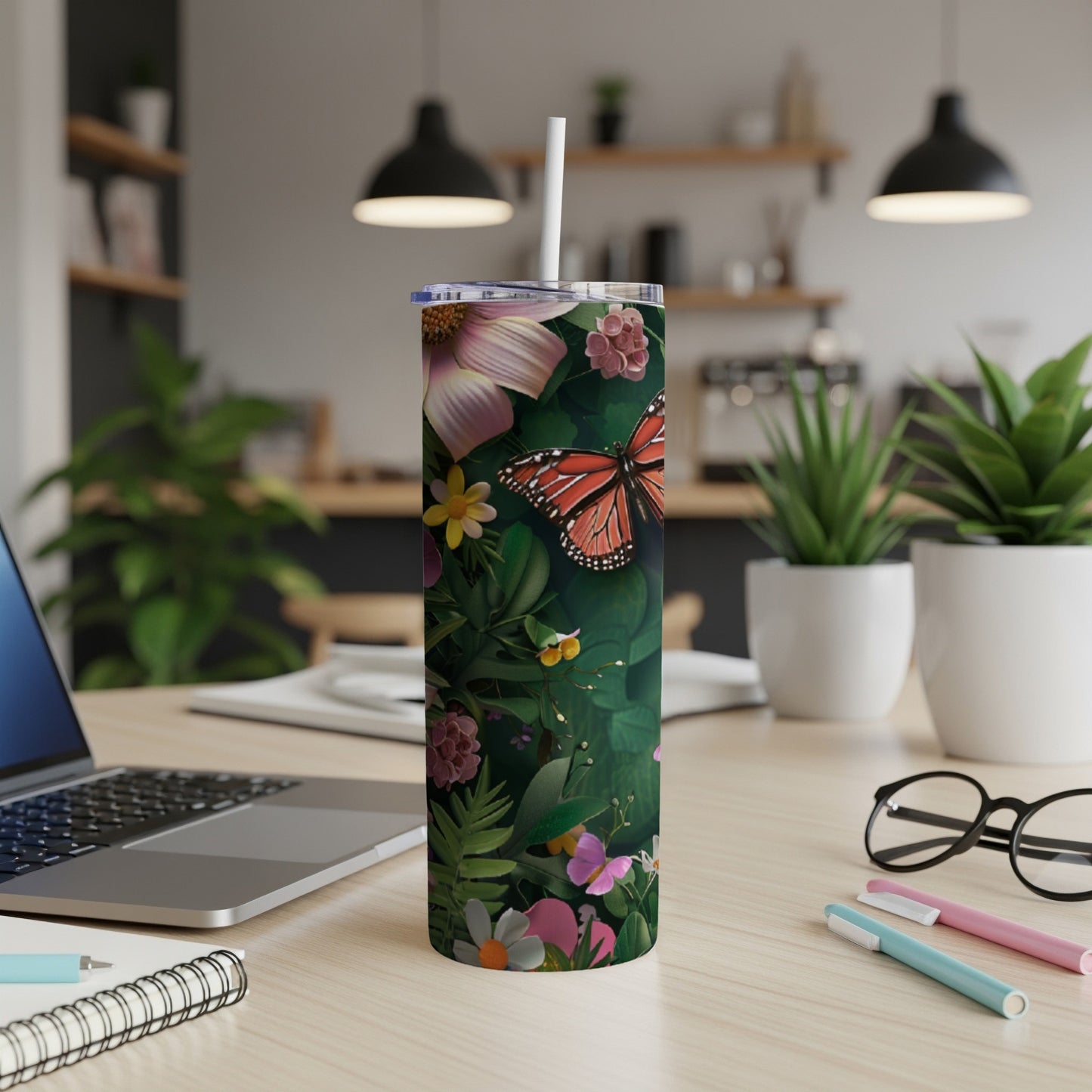 Floral tumbler with orange butterfly design on desk with laptop and pens.