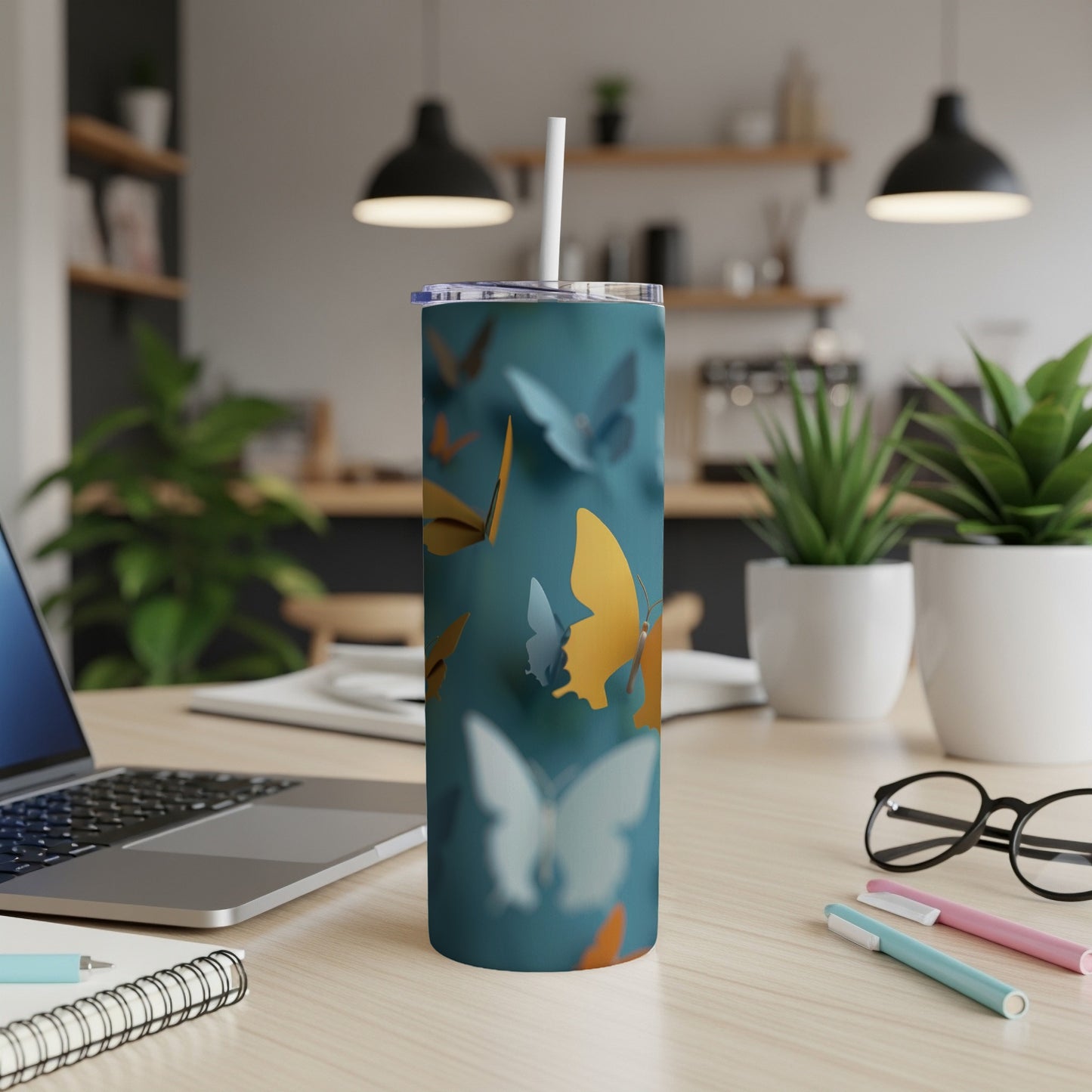 Blue tumbler with gold and orange butterflies, white straw, on a desk.
