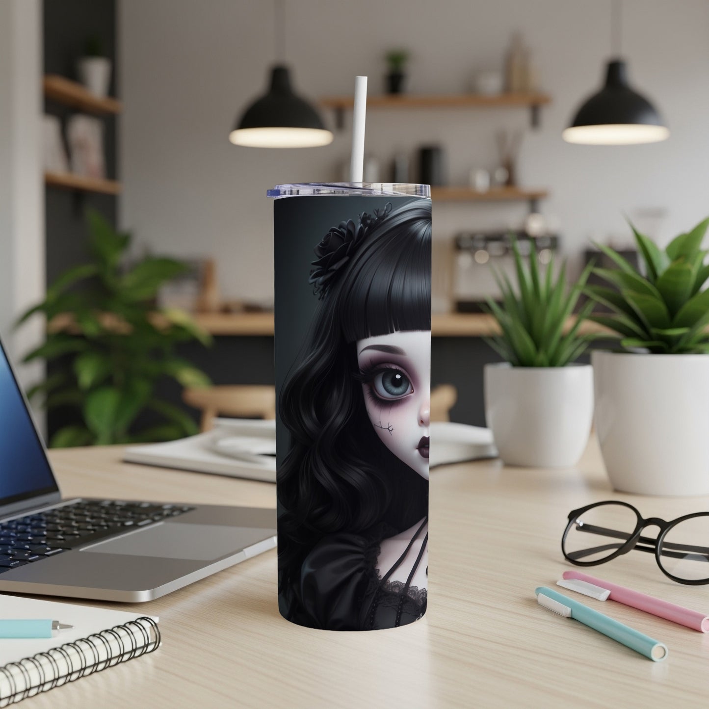 Gothic doll tumbler with straw on desk next to laptop and pens.