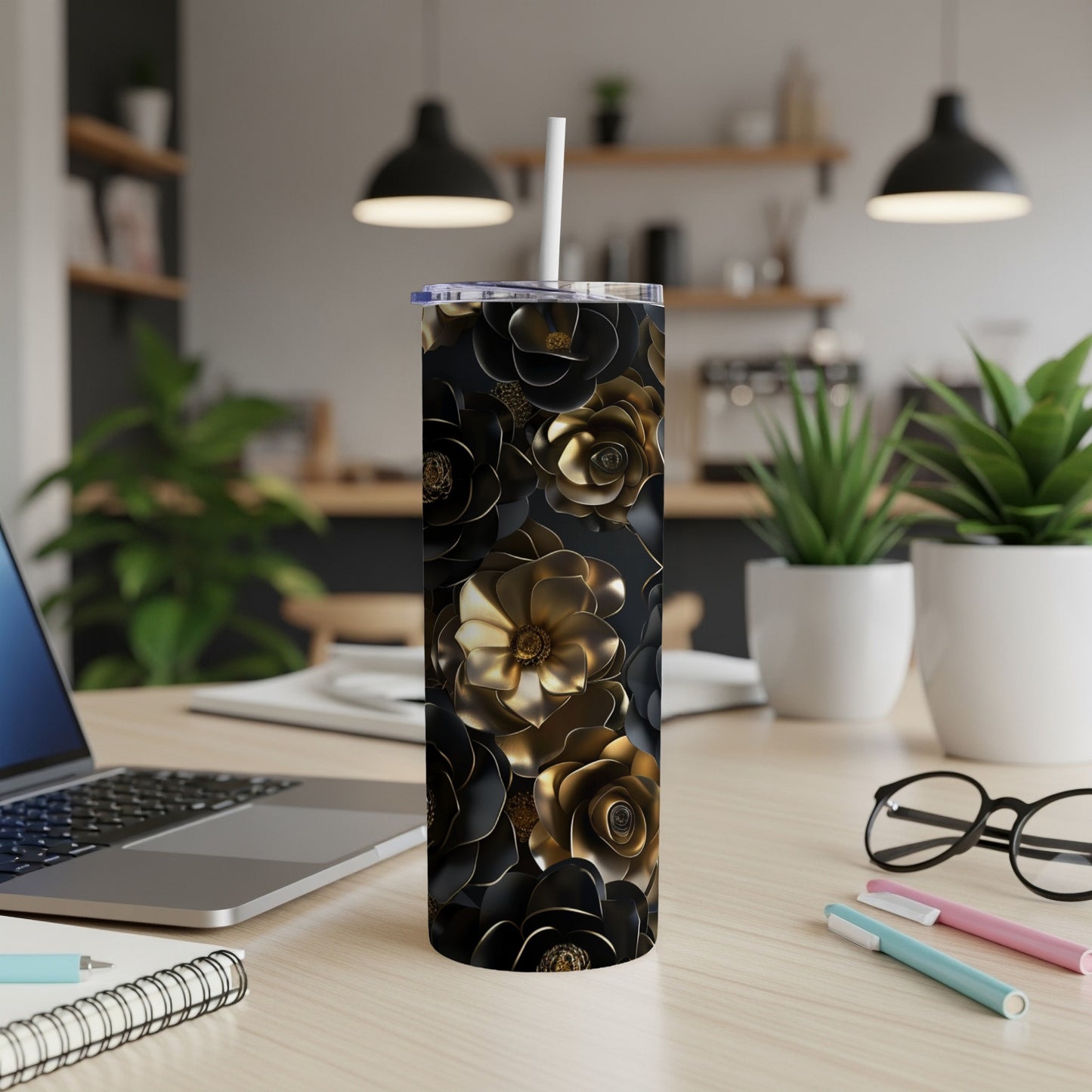 Black and gold floral tumbler with a white straw, on a desk.