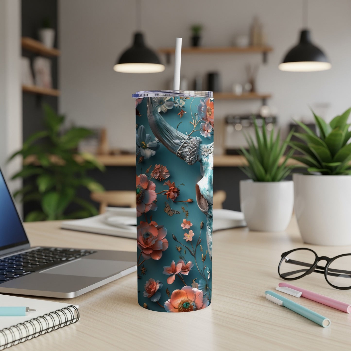 Teal floral tumbler with skull and straw on a desk.
