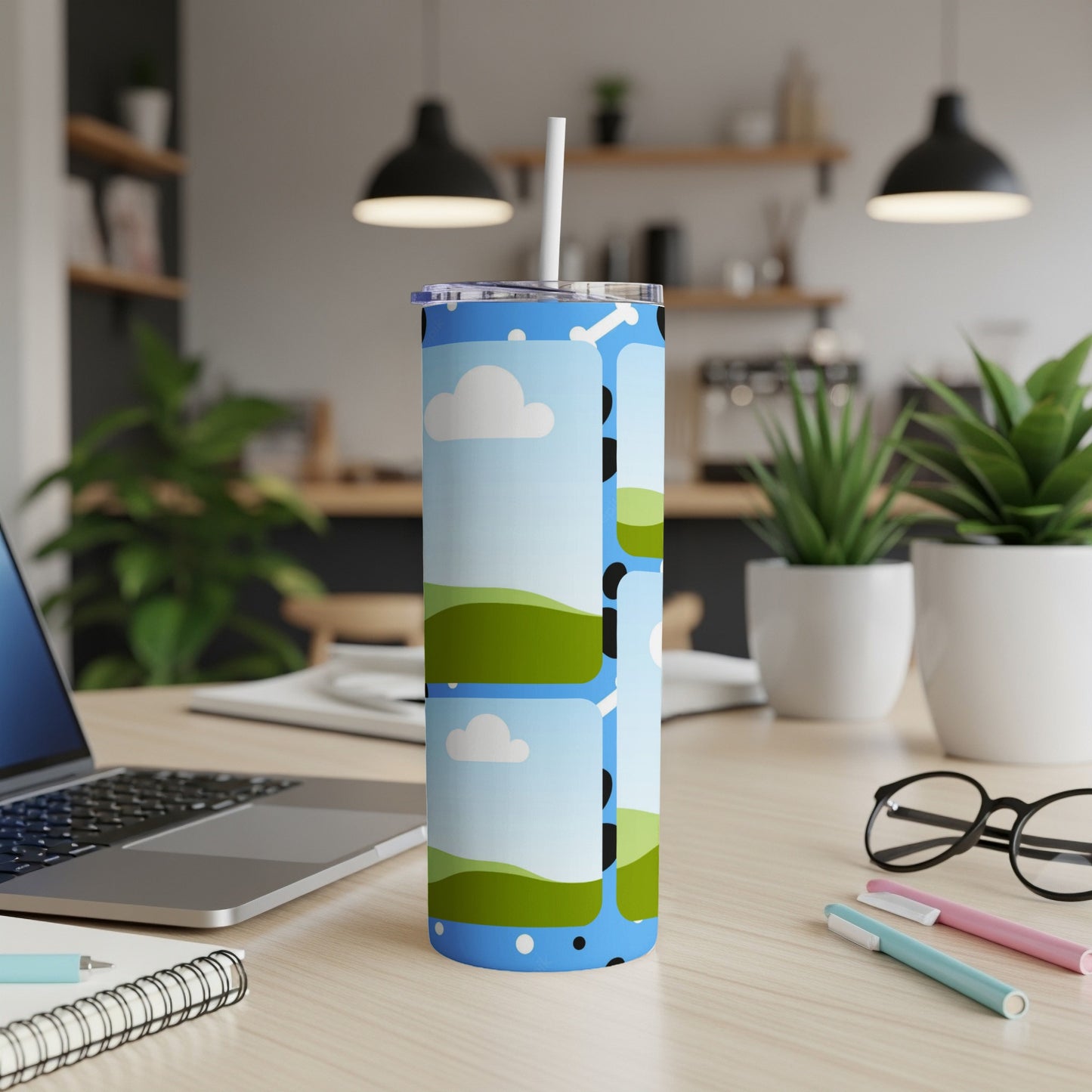 Blue tumbler with cartoon landscape and clouds, on a desk.