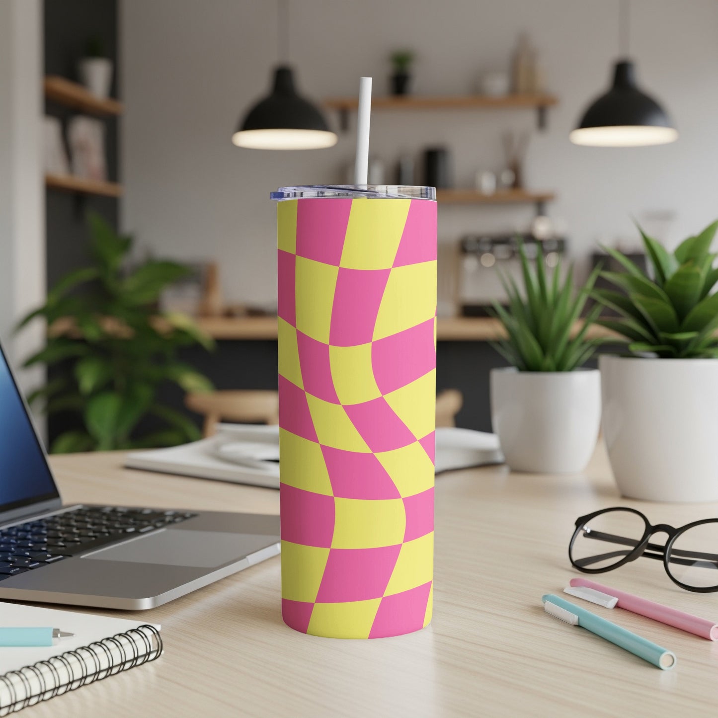 Pink and yellow checkerboard tumbler with a straw on a desk.