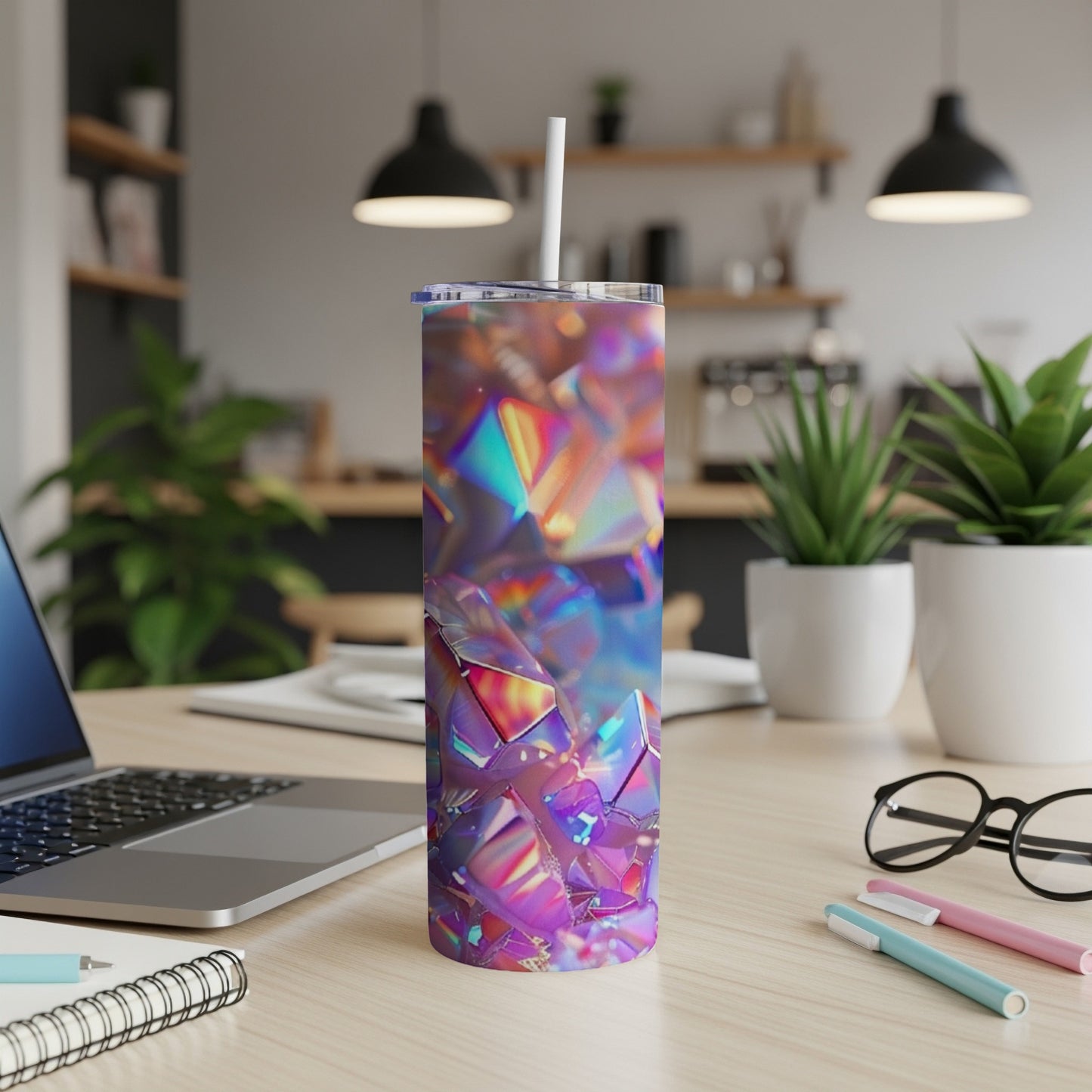 Holographic geometric tumbler with straw on desk next to laptop.