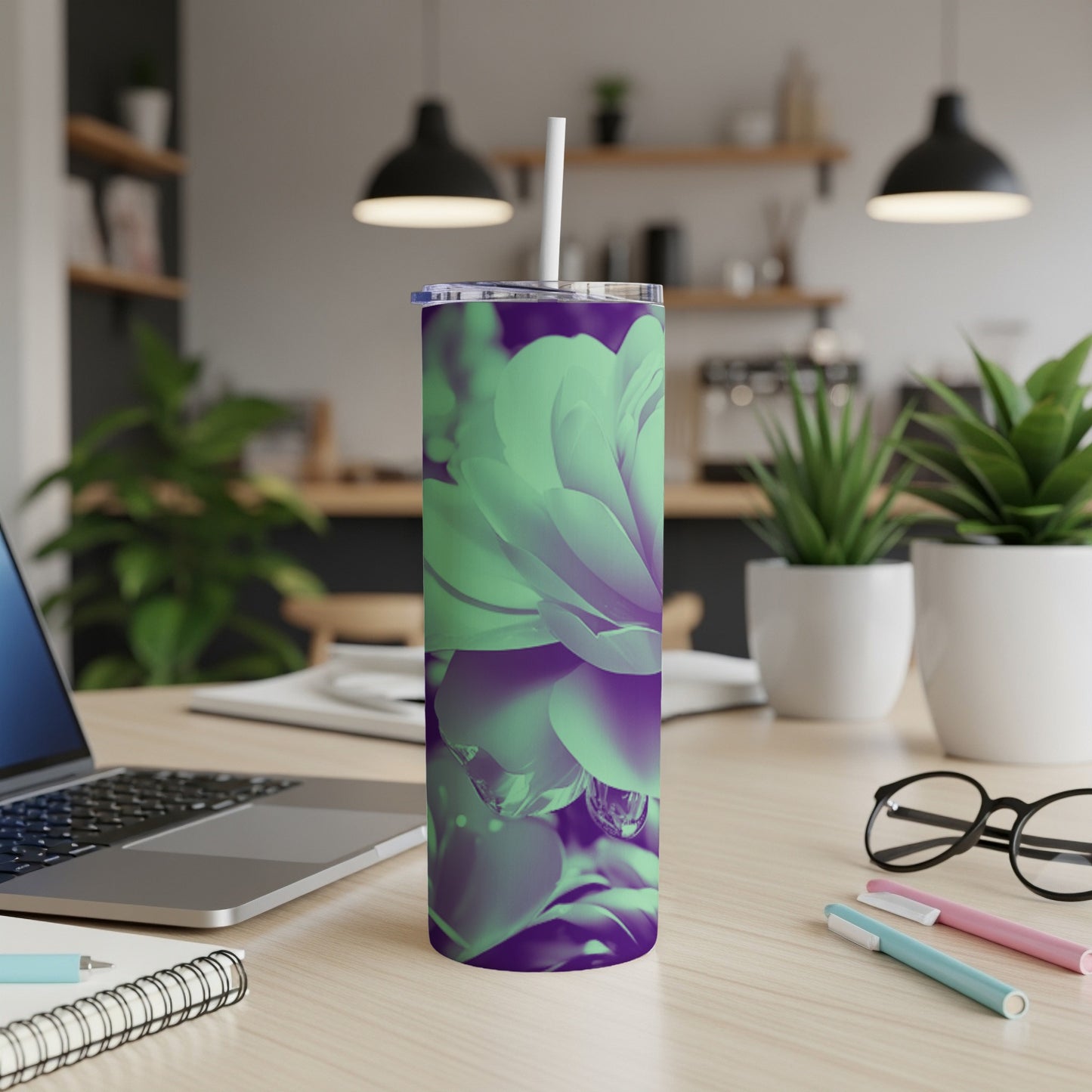 Green and purple floral tumbler with straw on a desk.