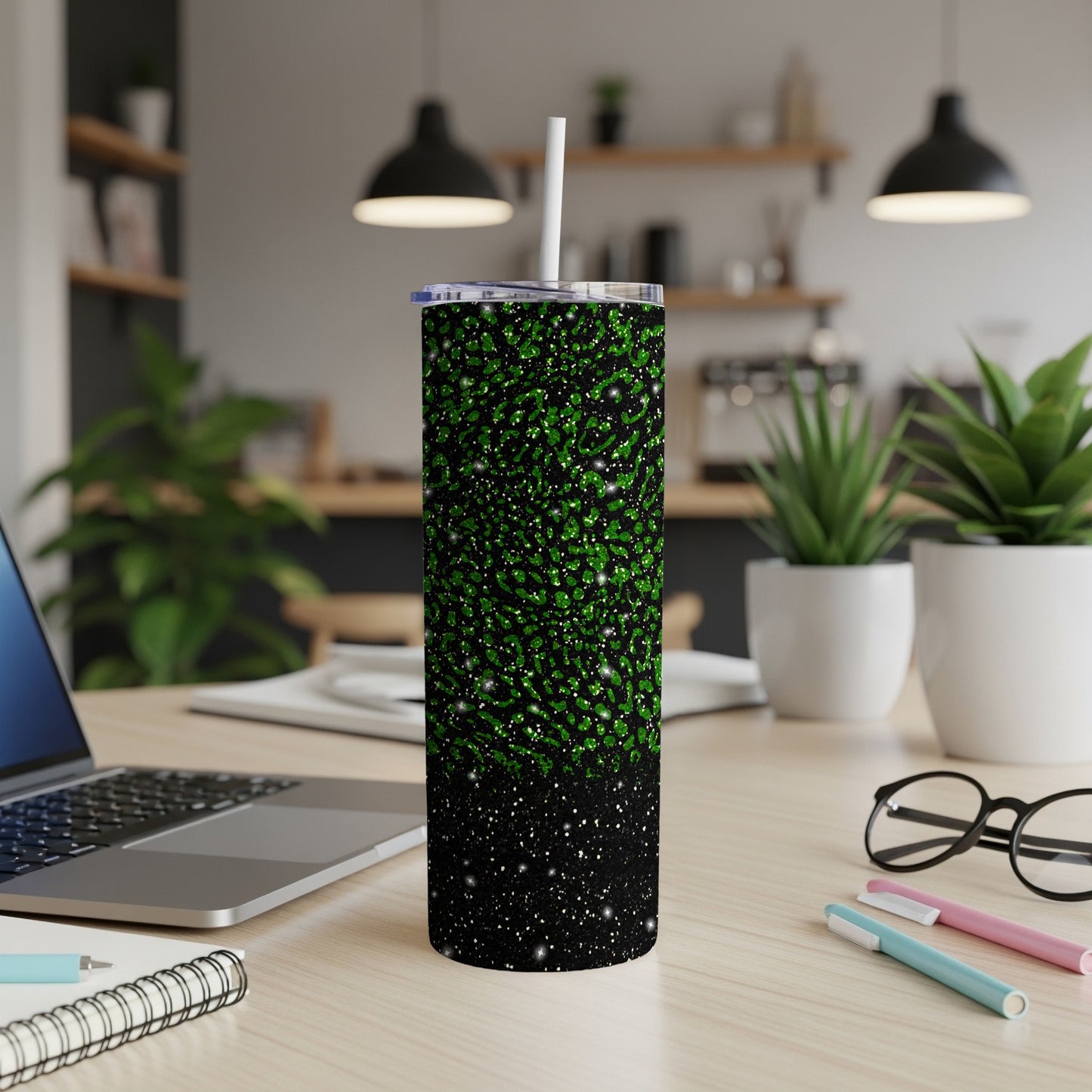 Green glitter tumbler with straw on a wooden desk.